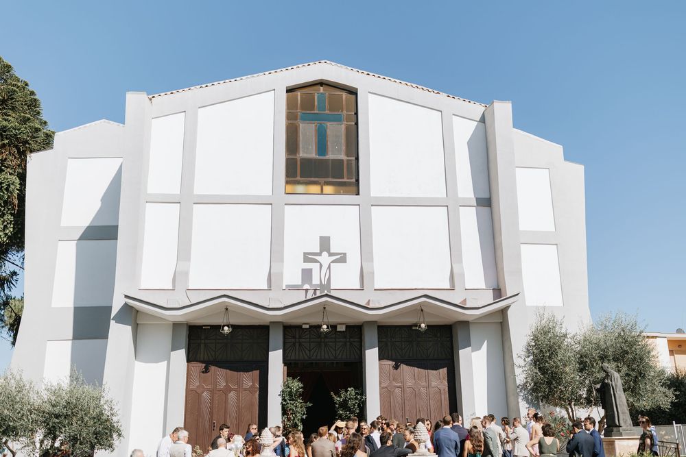 Modern white church building with arched windows and wooden doors photographed from multiple angles in bright daylight.