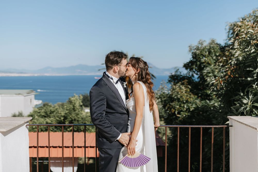 Couple embraces in romantic outdoor setting with ocean and mountain views during sunset ceremony.