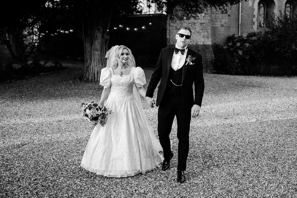 A wedding couple walks together on a gravel path in a black and white photograph.