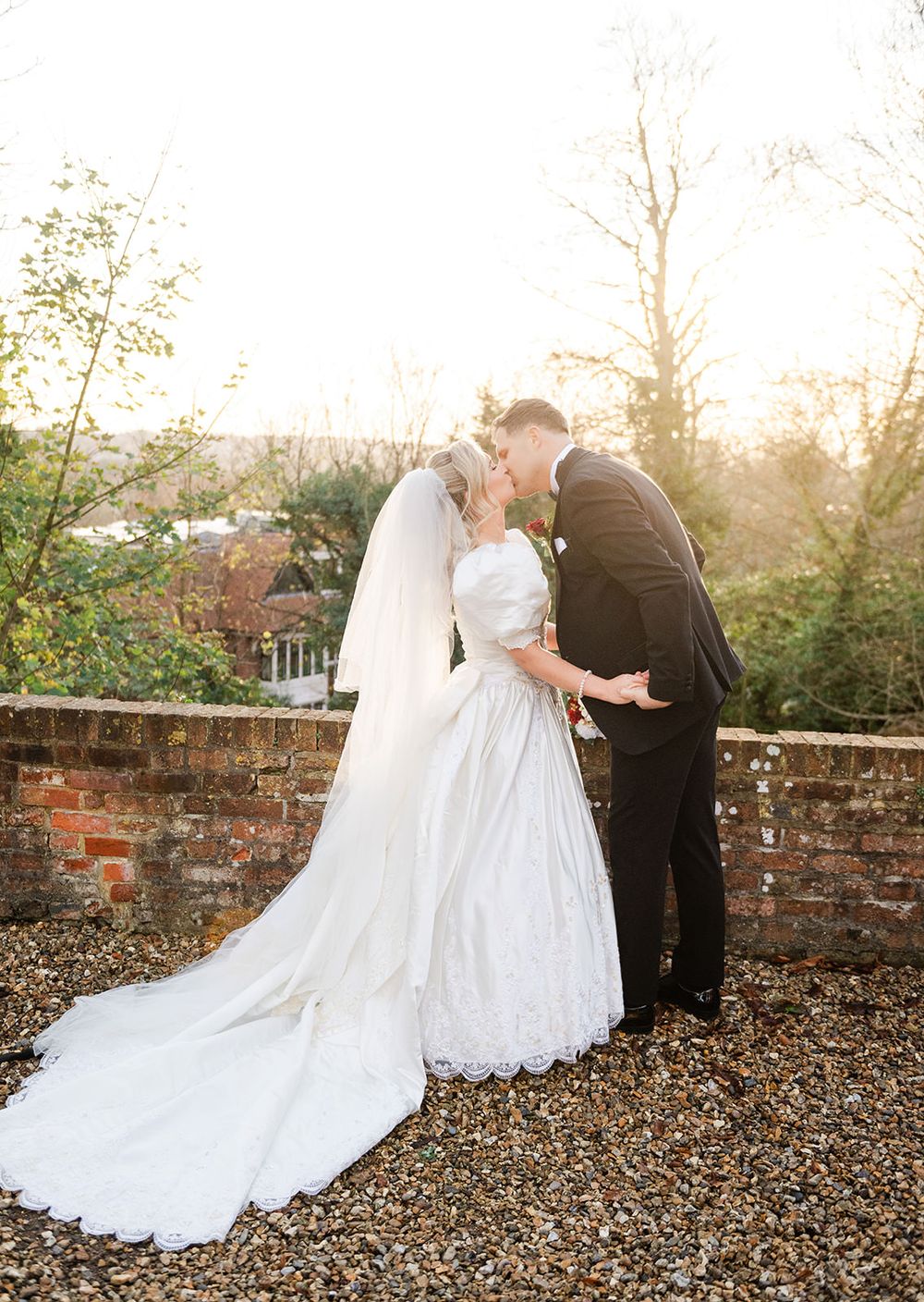 Romantic wedding couple shares intimate moment on autumn path with fallen leaves at sunset.