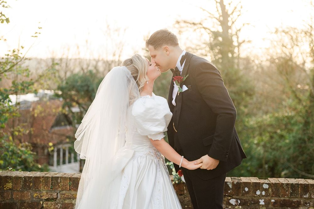A romantic wedding couple embraces in a garden setting during golden hour sunset.