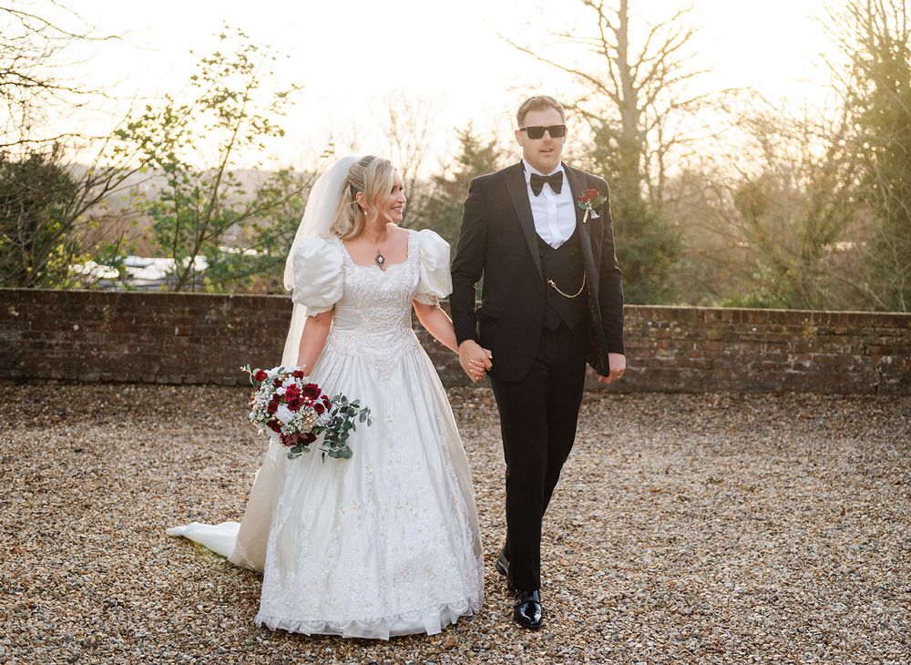 A wedding couple walks together on a gravel path during golden hour at sunset.