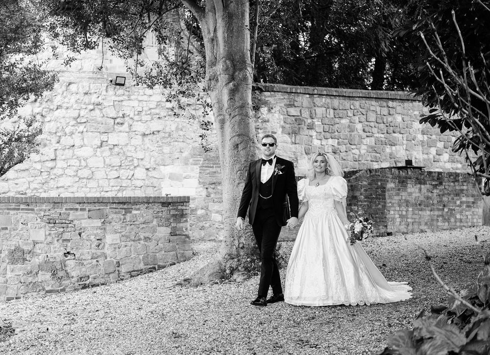 A series of black and white wedding photographs showing a couple walking through a garden with stone walls.