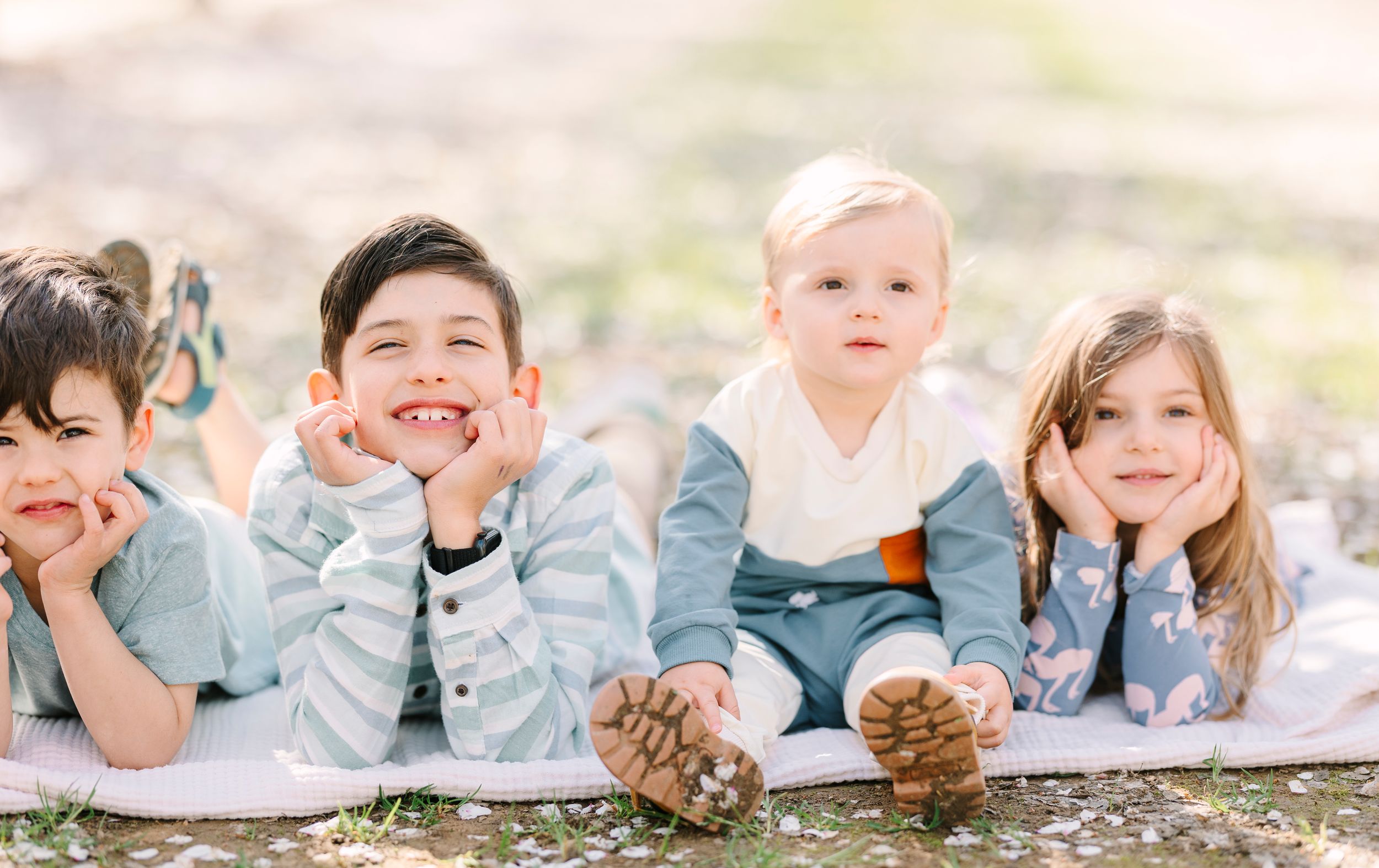 Family lying on a blanket outdoors enjoying a playful moment together in casual attire.