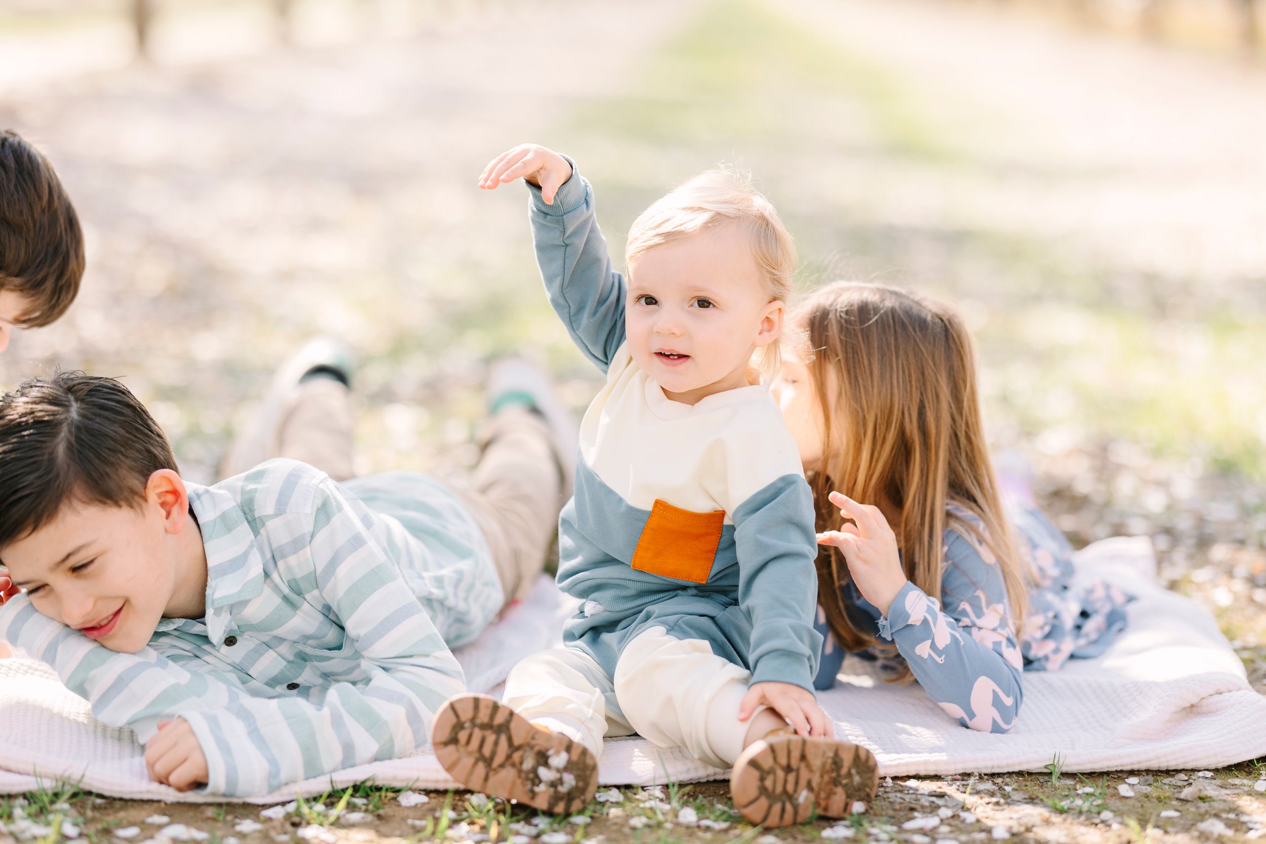 Children playing and laughing while lying on a blanket in an outdoor setting.