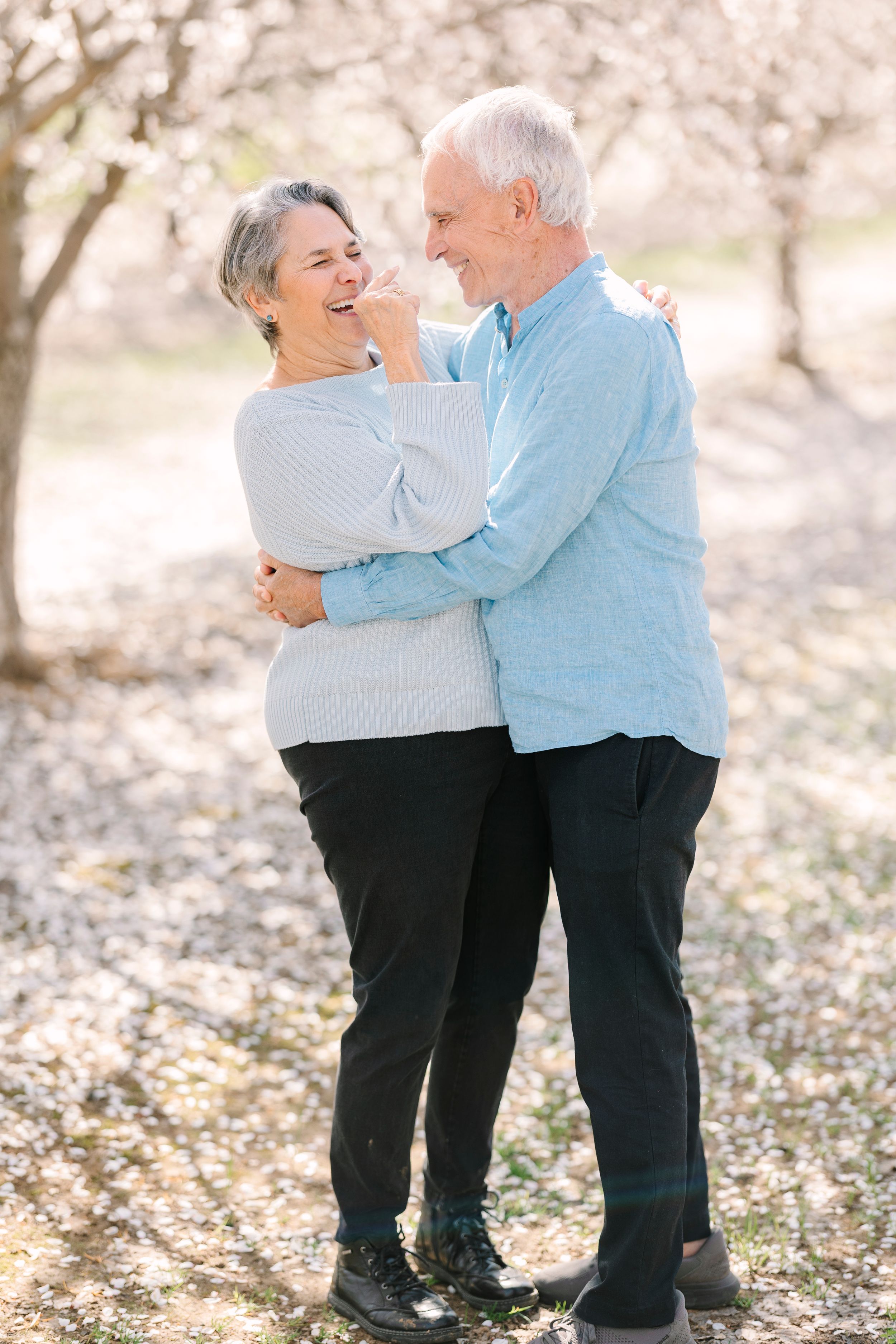 Elderly couple in matching light blue sweaters embracing outdoors among fallen leaves.