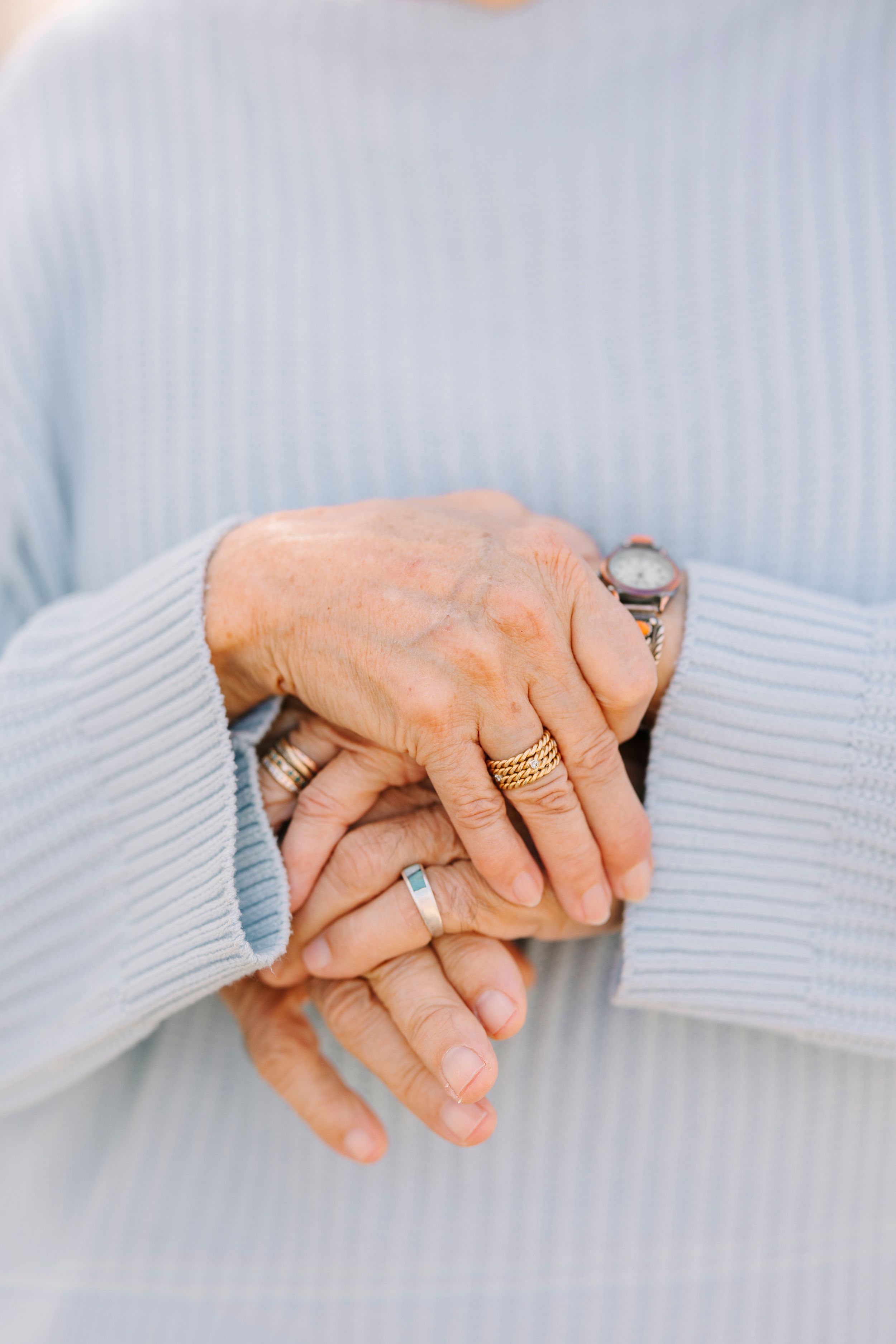 Close-up of elderly couple's hands holding each other, showing wedding rings and blue sweaters.
