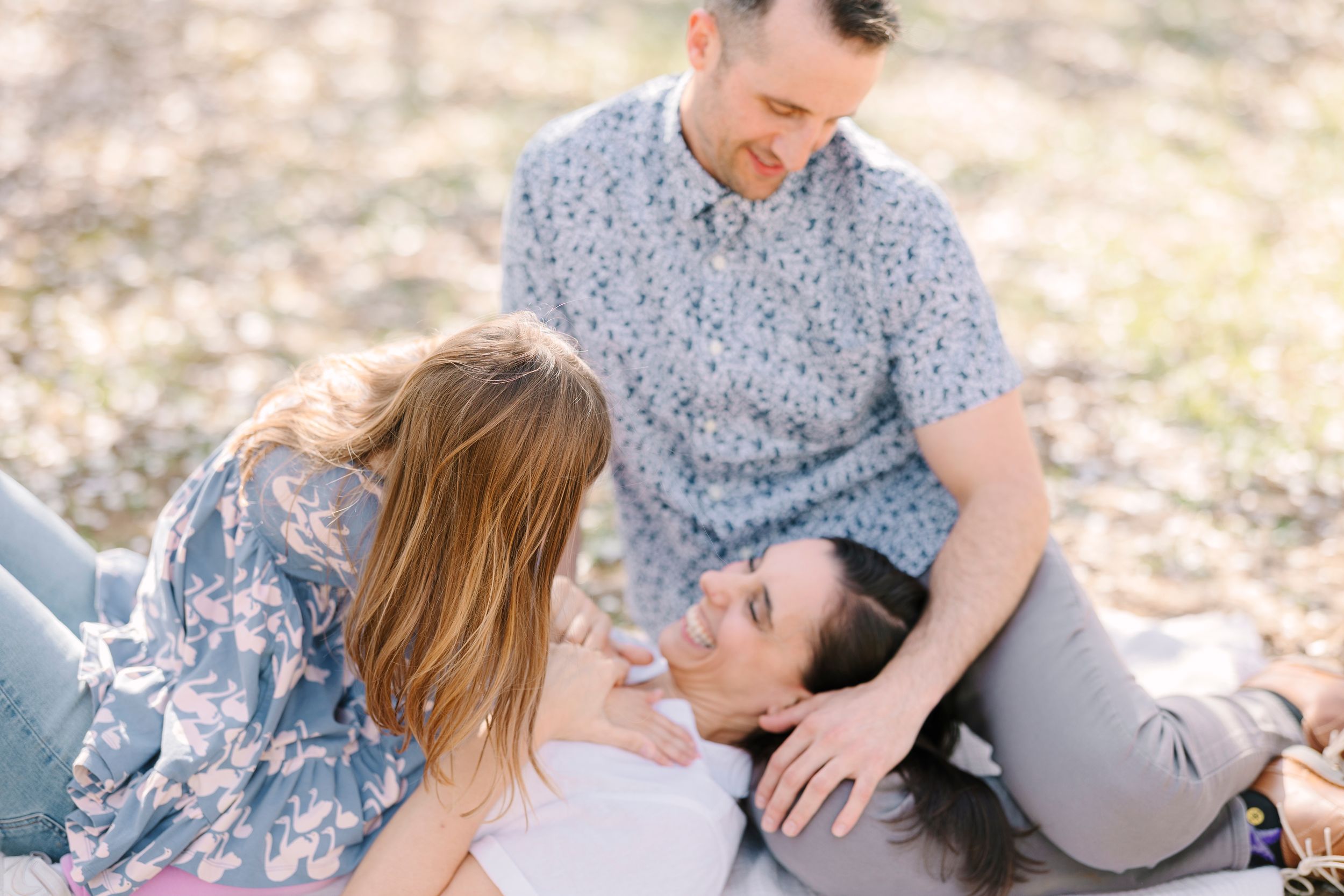 Family members lying on blanket outdoors sharing intimate moments together.