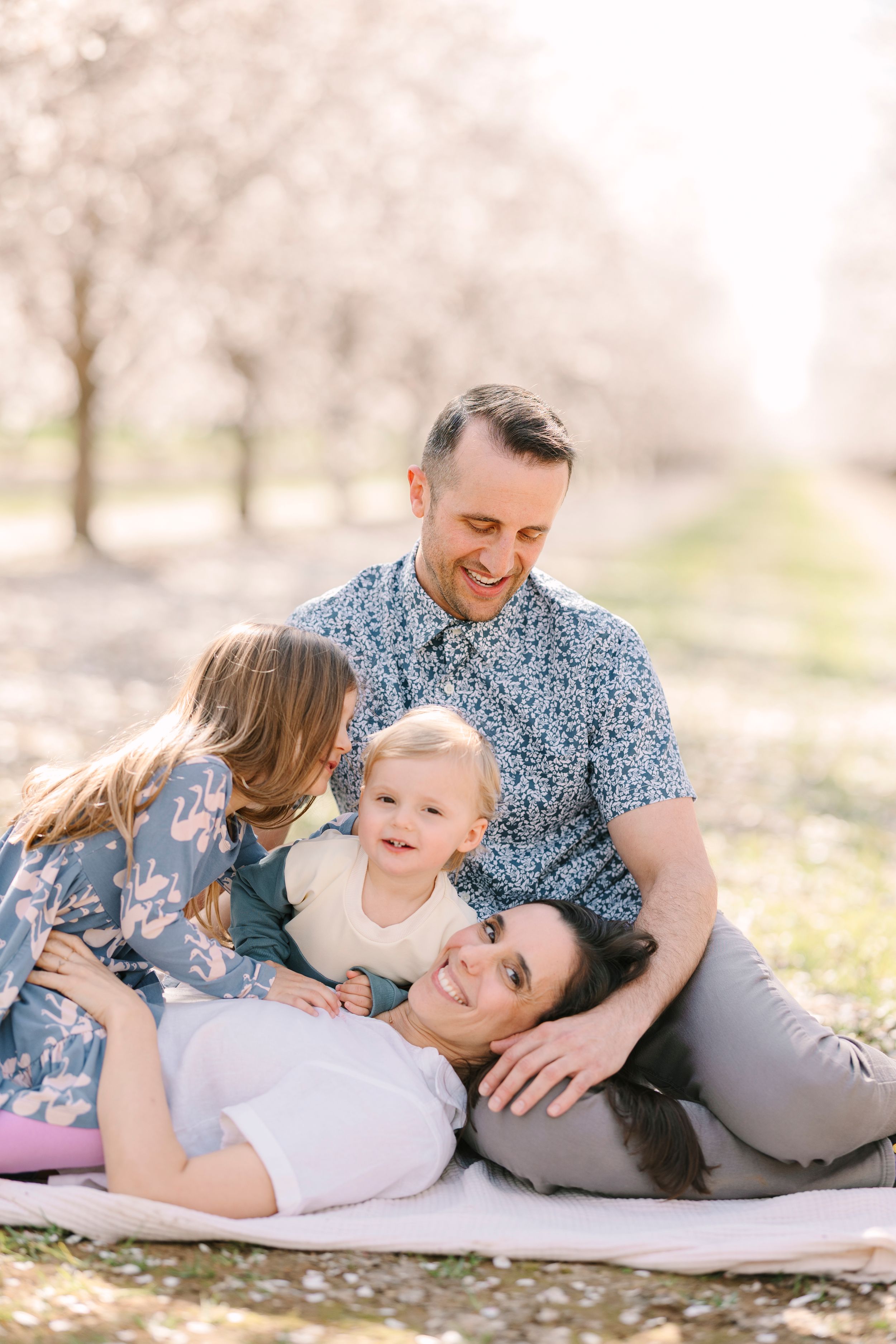 Family of four lying on blanket outdoors sharing joyful moments together.