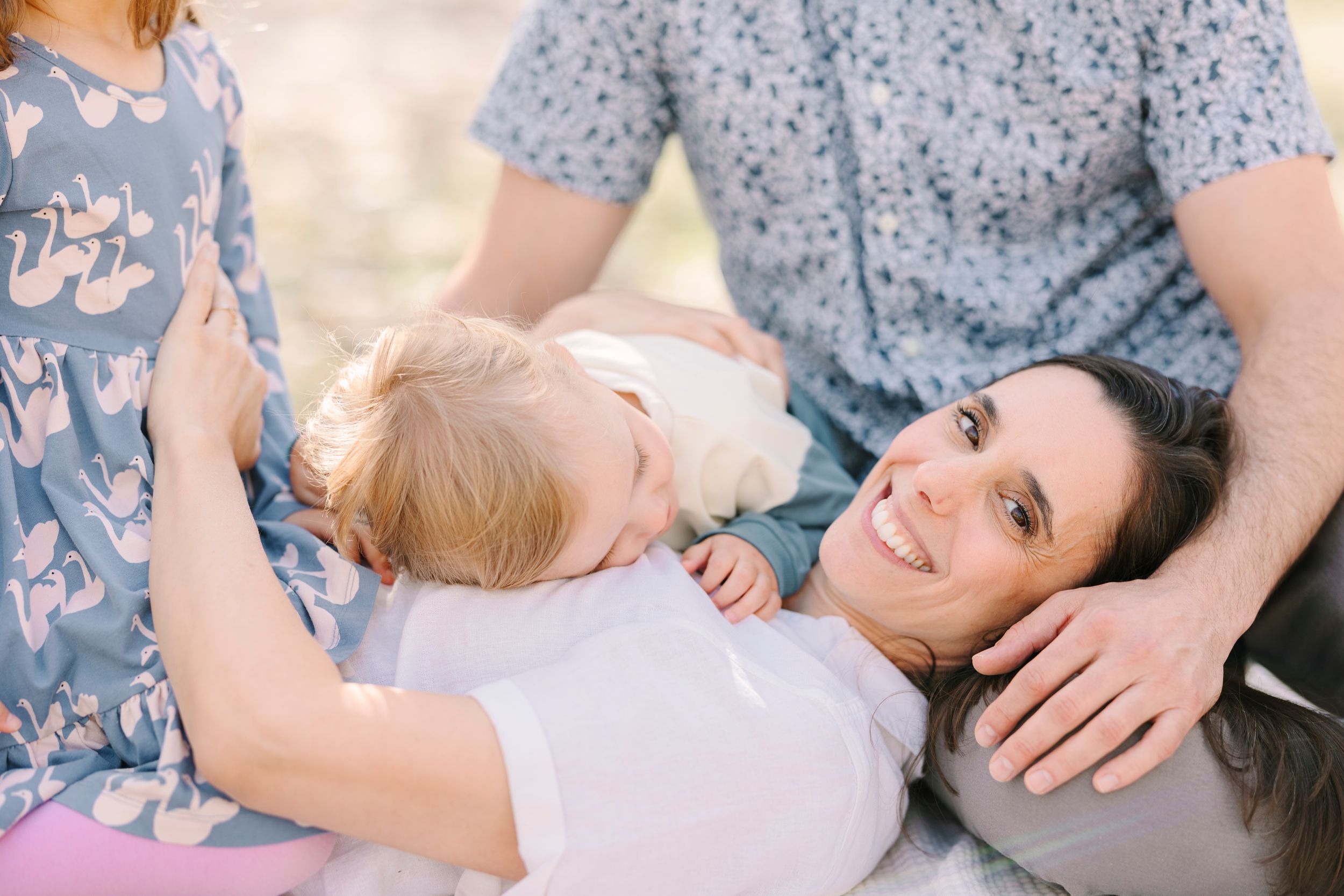 Family relaxing on blanket outdoors sharing intimate moments together.