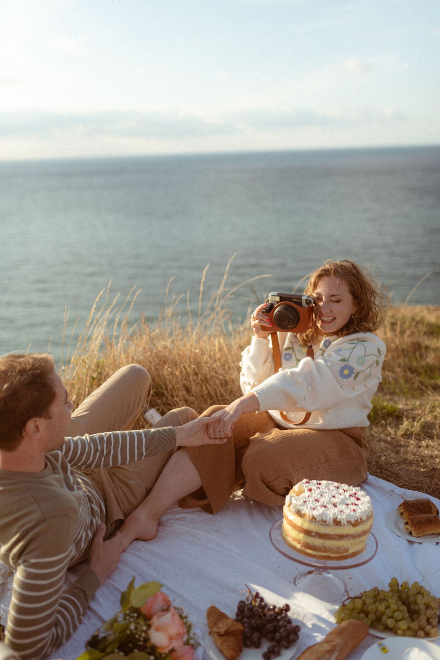 Romantic picnic by the ocean with cake and refreshments on a sunny day.