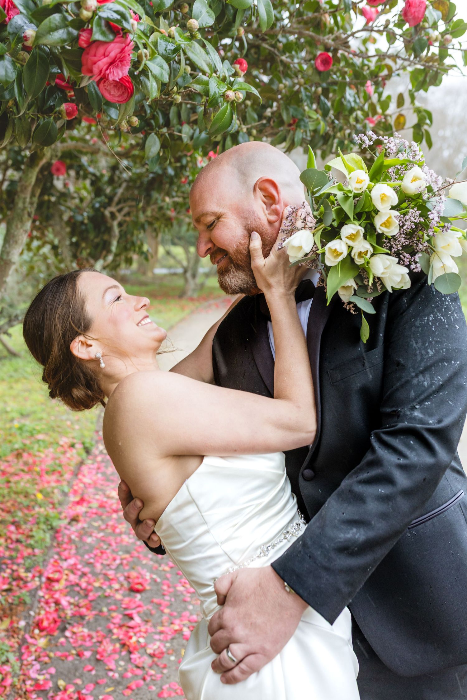 Romantic couple embraces and kisses in a garden with red roses and white flowers.