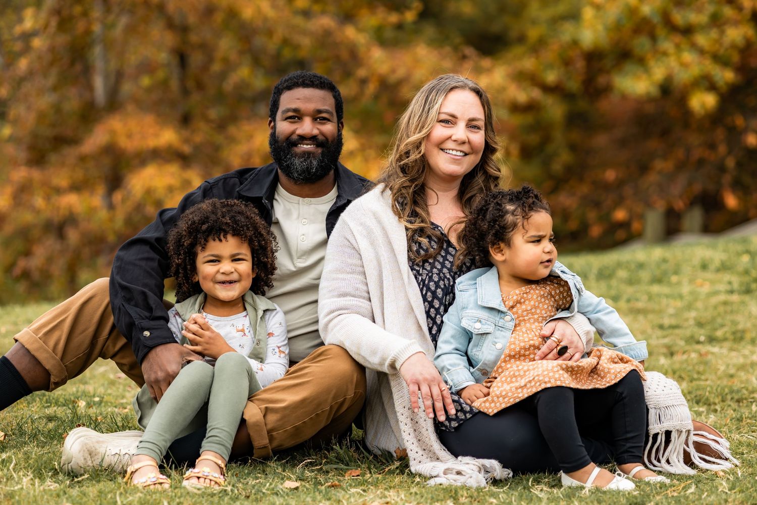 Family enjoying a fall day together laying in autumn leaves during an outdoor photo session.