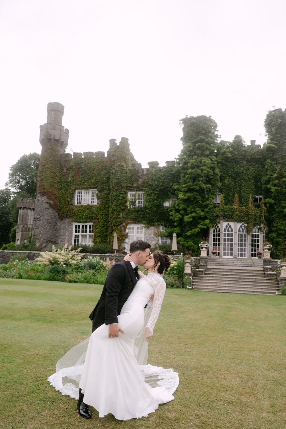 A romantic wedding couple dances and embraces on the expansive lawn of a historic castle estate.