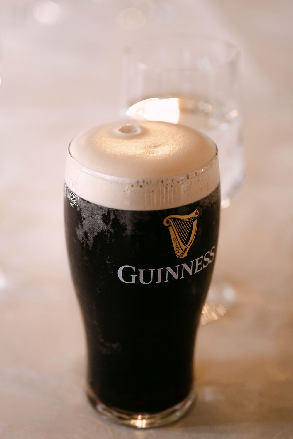 A freshly poured pint of Guinness stout beer with creamy foam head in branded glass against light background.