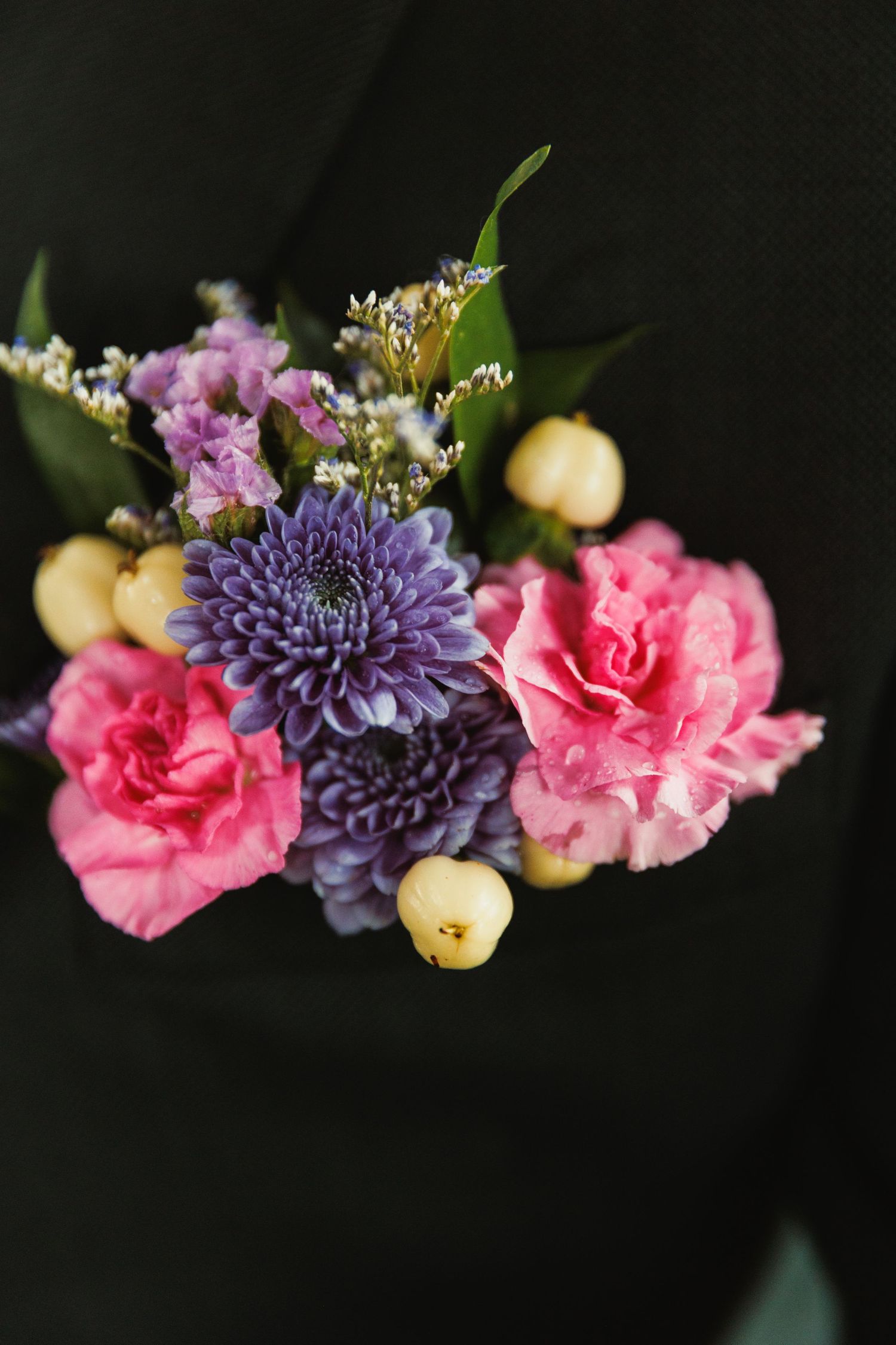 Floral arrangement with purple dahlia, pink carnations and yellow accents against black background.