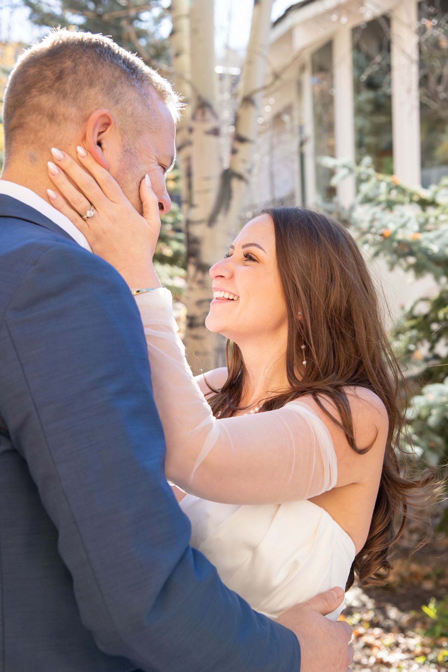 A romantic moment between newlyweds embracing outdoors on their wedding day with sunlit trees in the background in Vail Colorado
