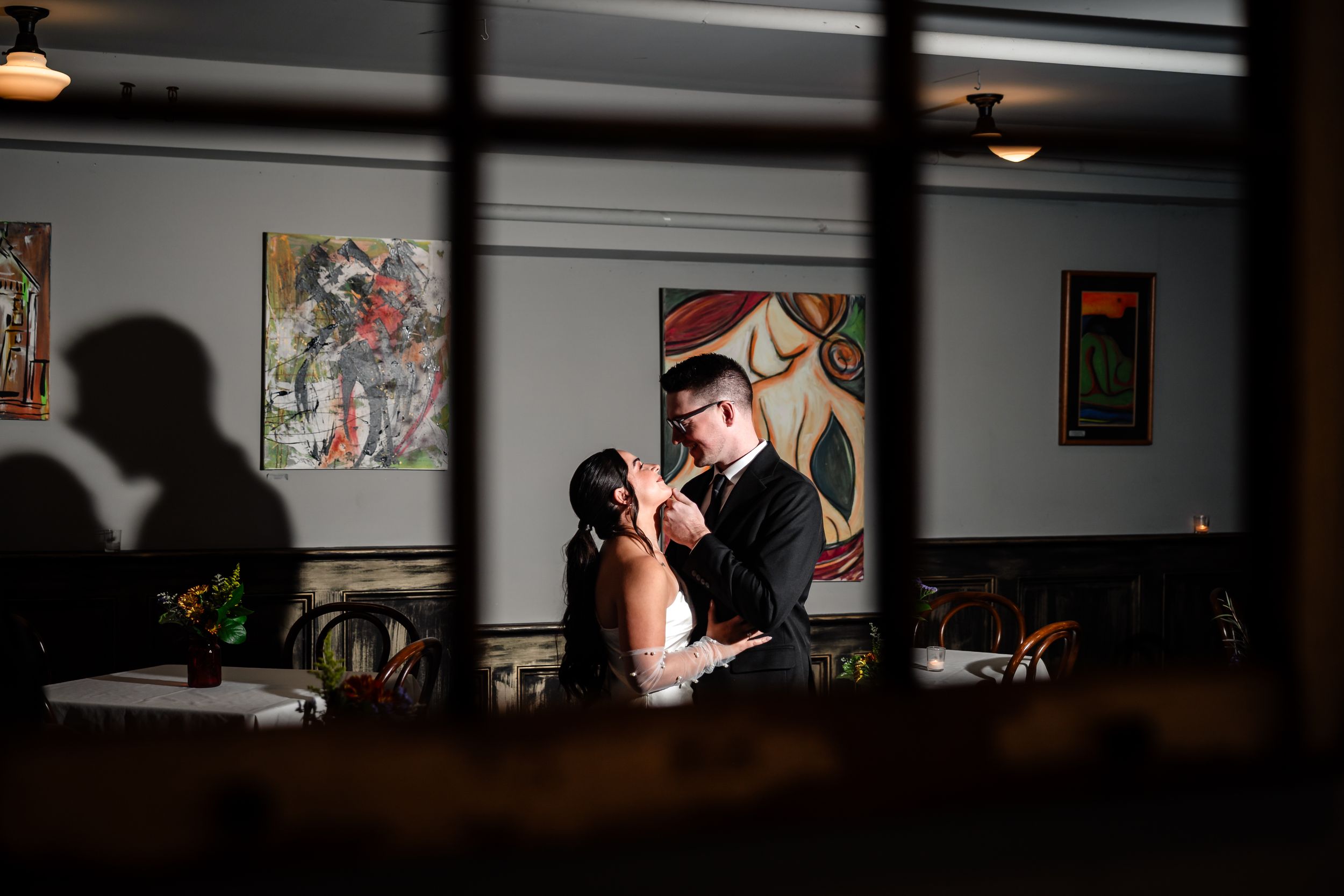 A couple shares an intimate moment in a dimly lit bar interior with vintage decor and pendant lighting.