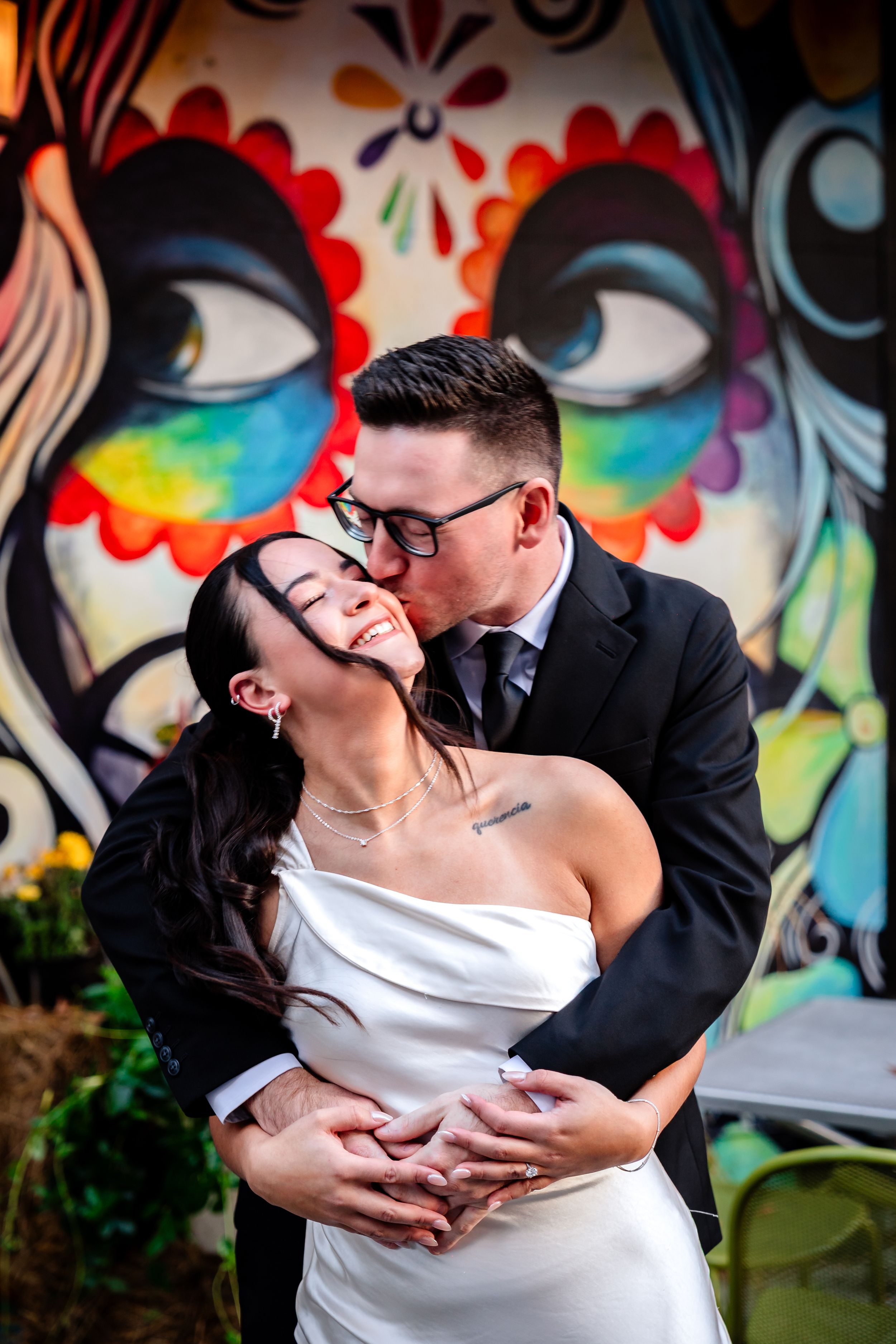 Romantic couple shares passionate kisses against colorful graffiti wall backdrop.