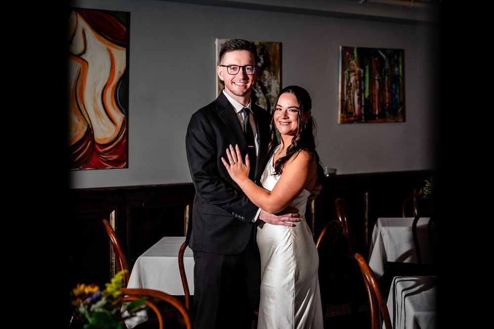 A couple shares an intimate dance moment at their wedding reception in a dimly lit room with art on the walls.