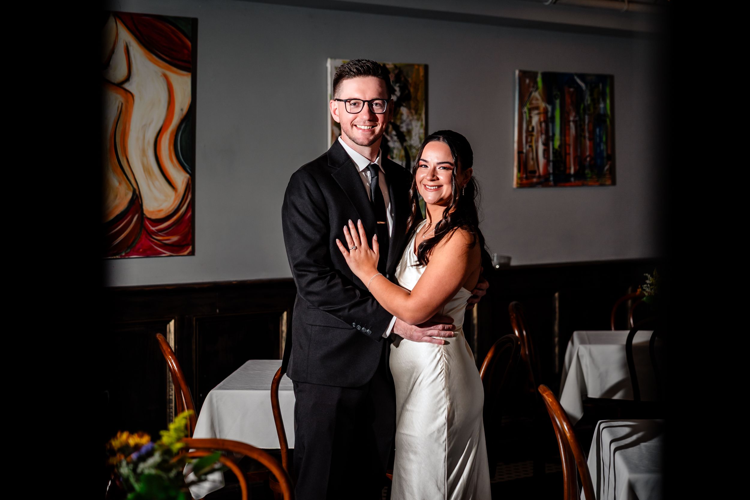 A couple shares an intimate dance moment at their wedding reception in a dimly lit room with art on the walls.