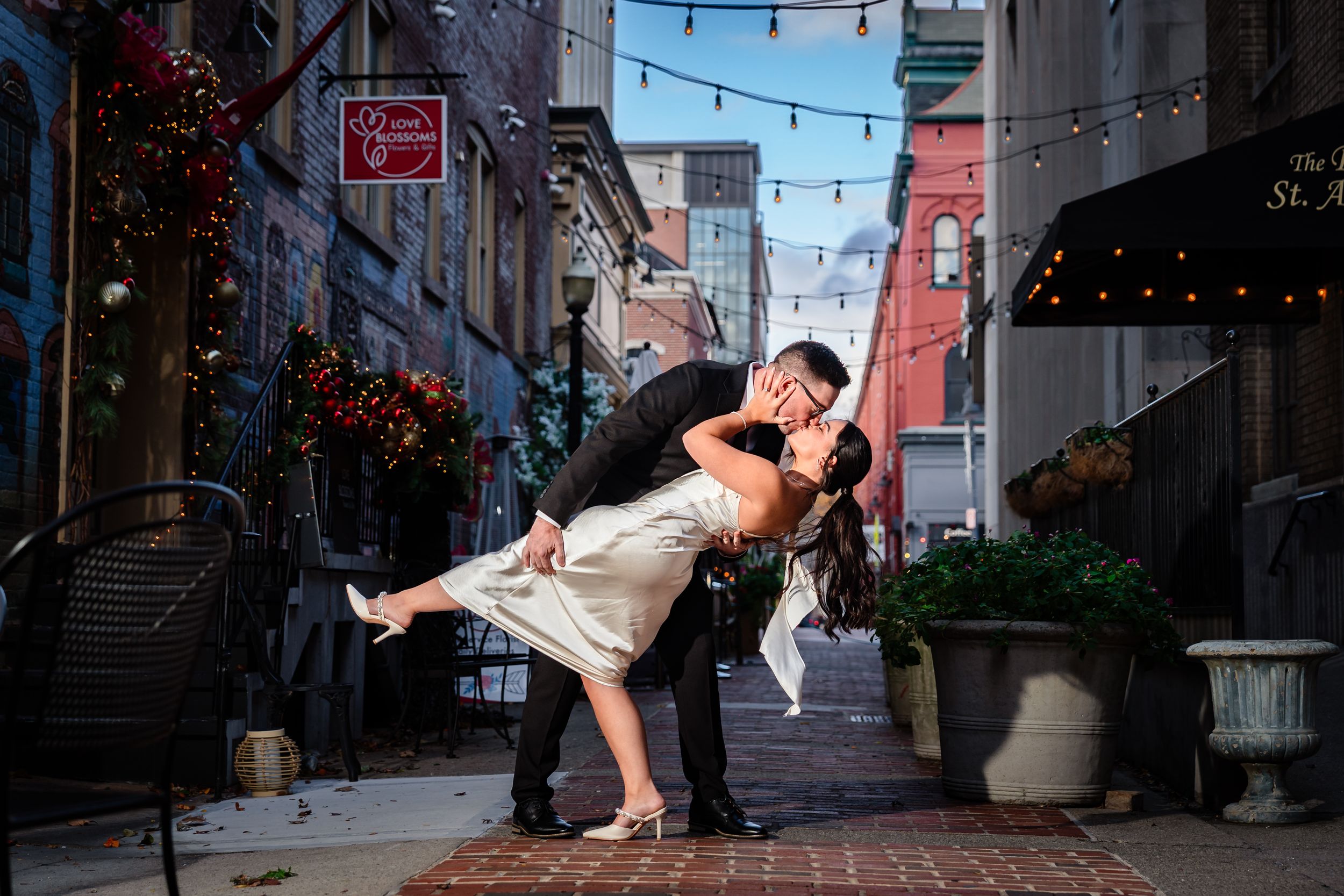 Romantic dance poses in an urban alley with string lights overhead.