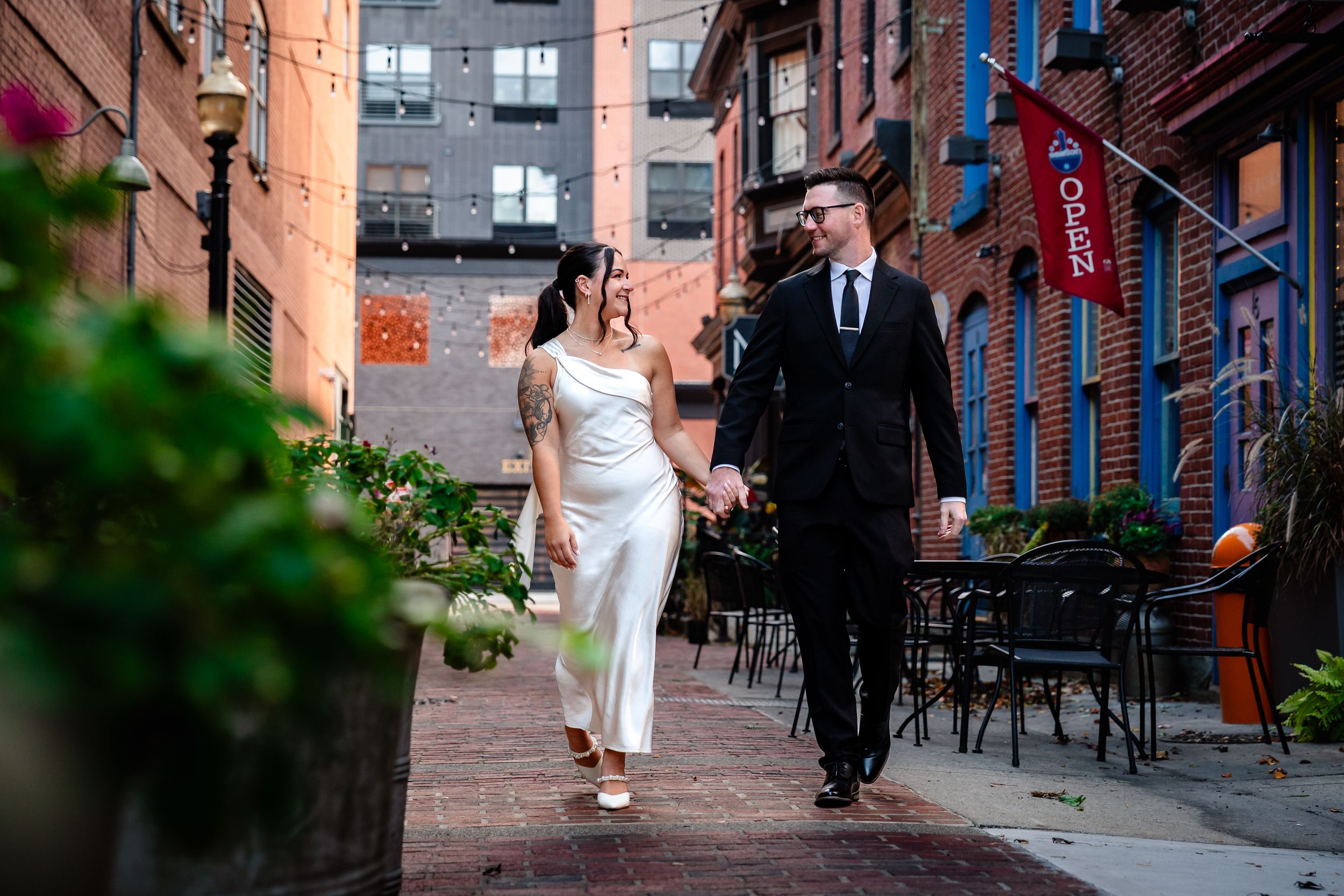 Couple walks hand in hand down urban alley with brick buildings.