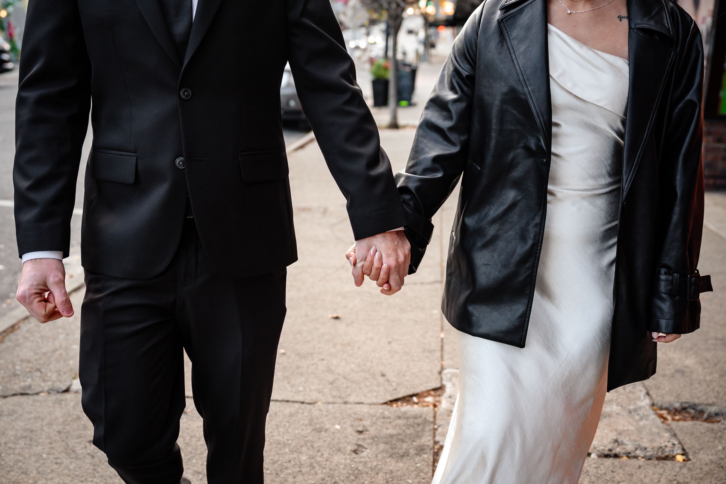 Couple in formal attire holds hands while walking outdoors.