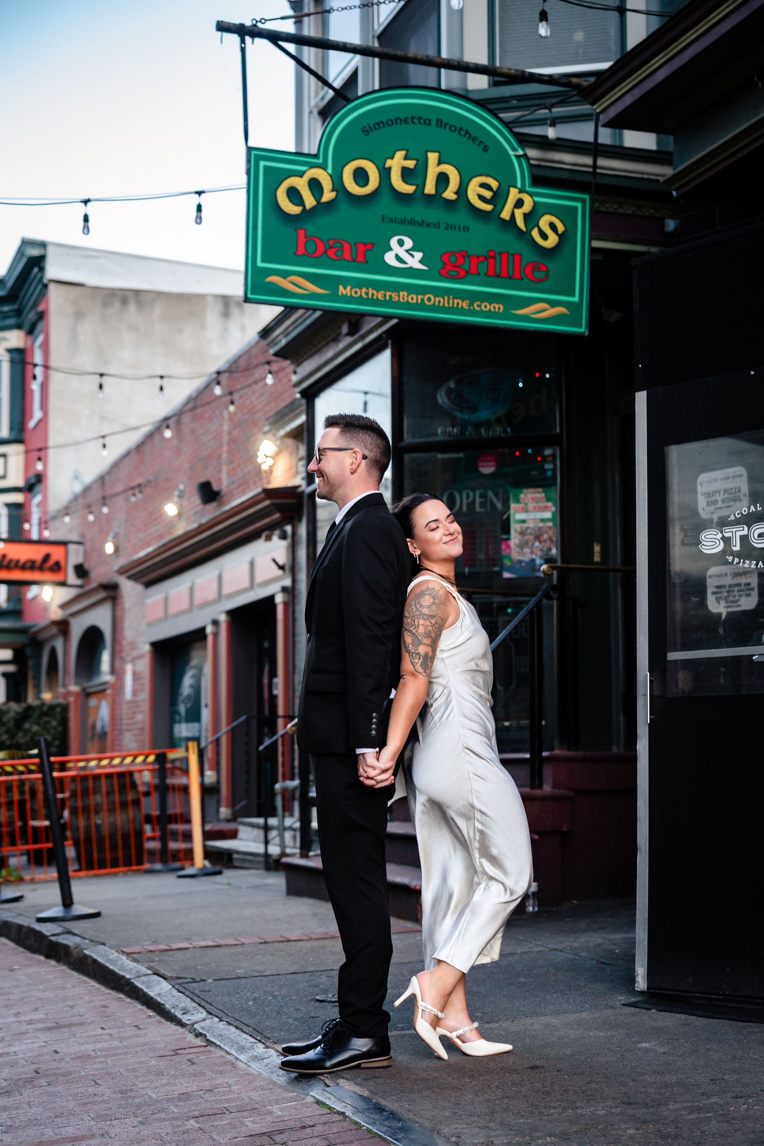 A couple embraces outside a storefront with illuminated green signage at dusk.