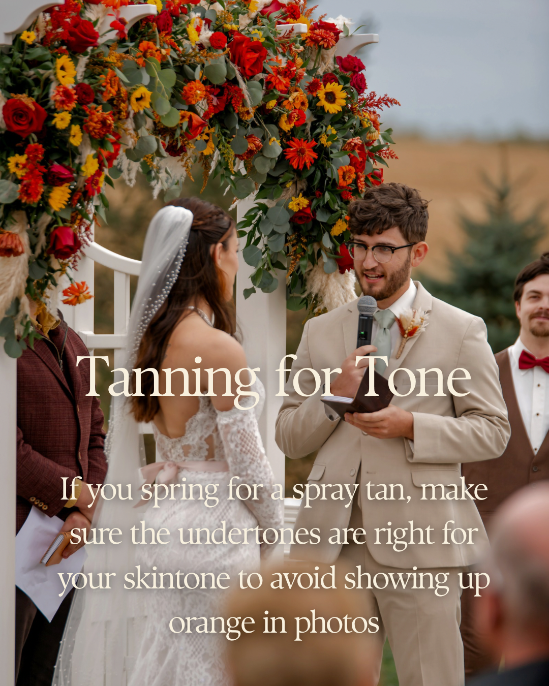 Floral wedding arch with red and orange flowers decorates an outdoor ceremony space during a fall celebration.