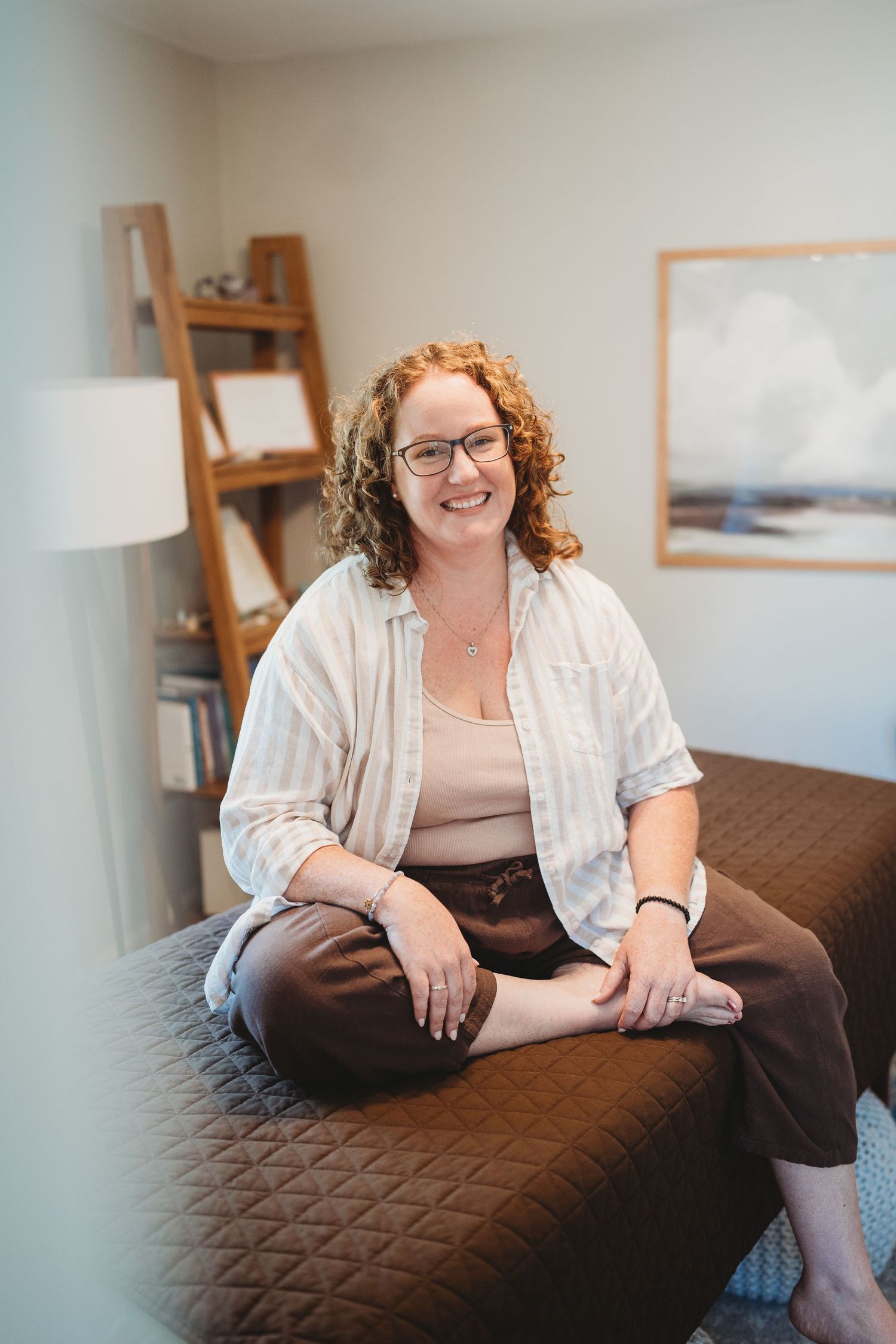 A person in casual attire sits comfortably on a dark quilted couch in a bright, minimalist room setting.