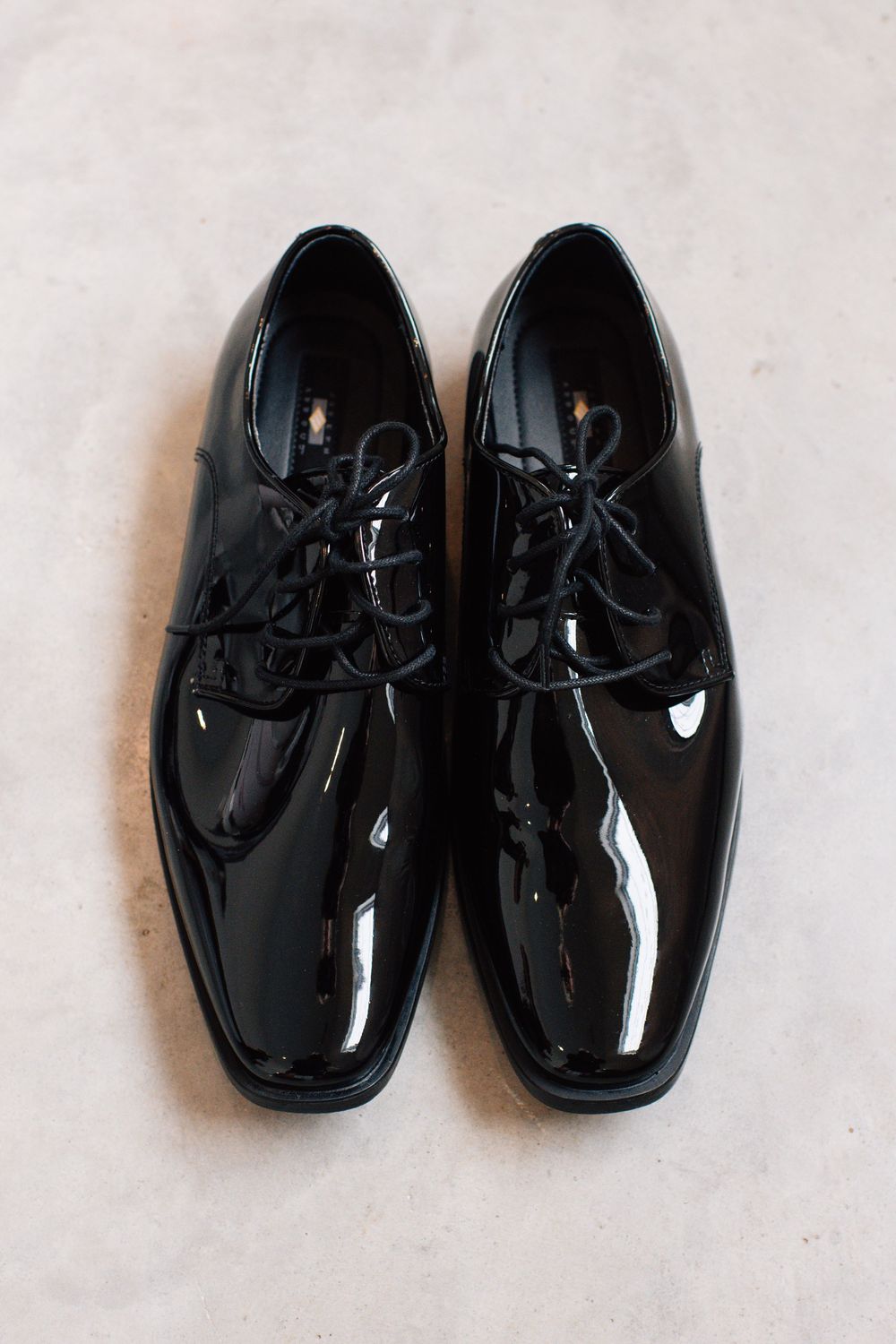 Shiny black patent leather dress shoes arranged in a row against a white background.