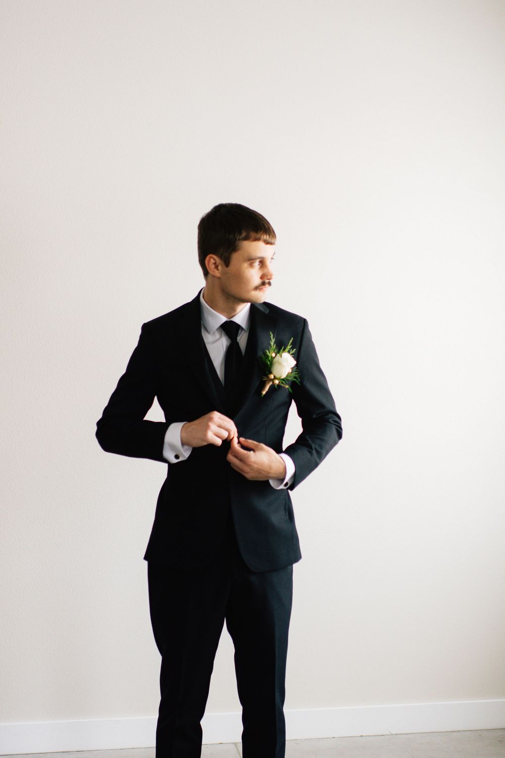 Figure in black formal suit striking playful poses against white backdrop.