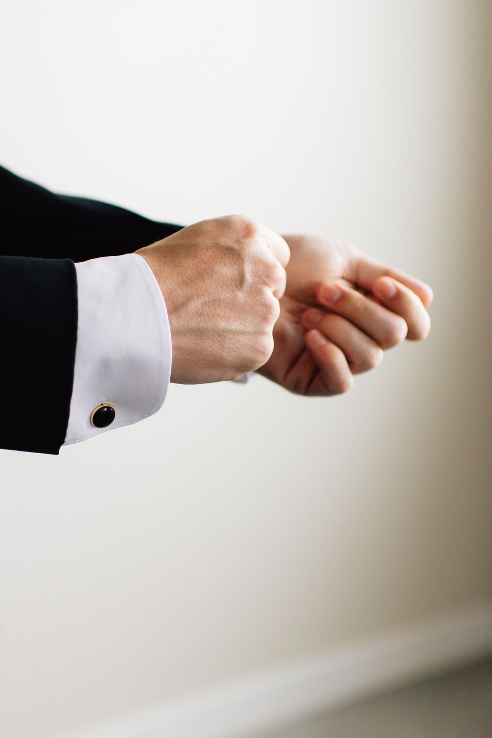 Close-up of hands in white dress shirt cuffs adjusting cufflinks.