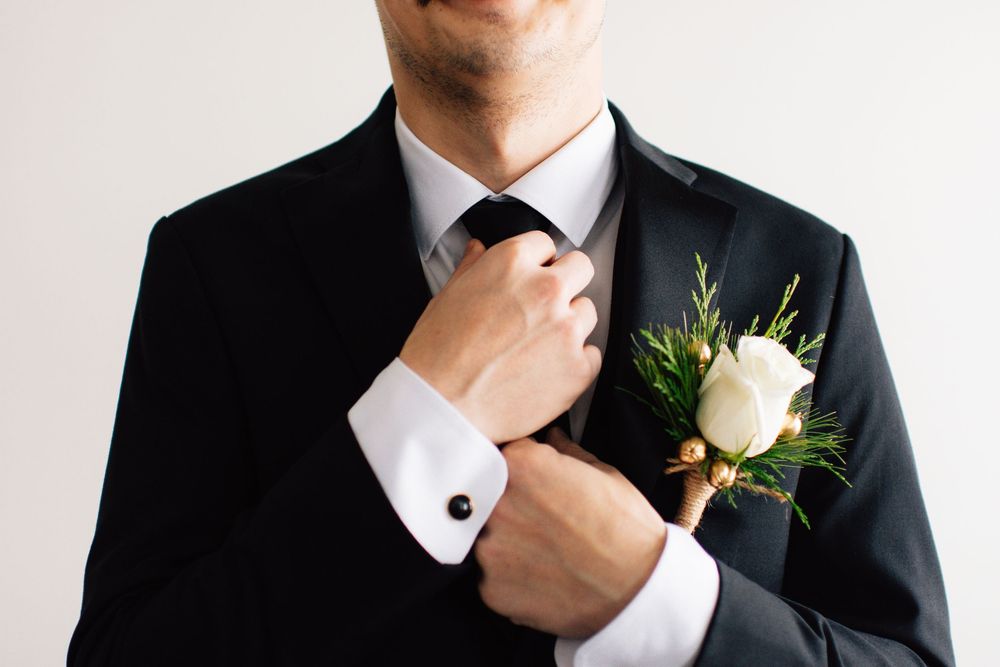 Close-up details of groom's formal attire with white boutonniere against light background.