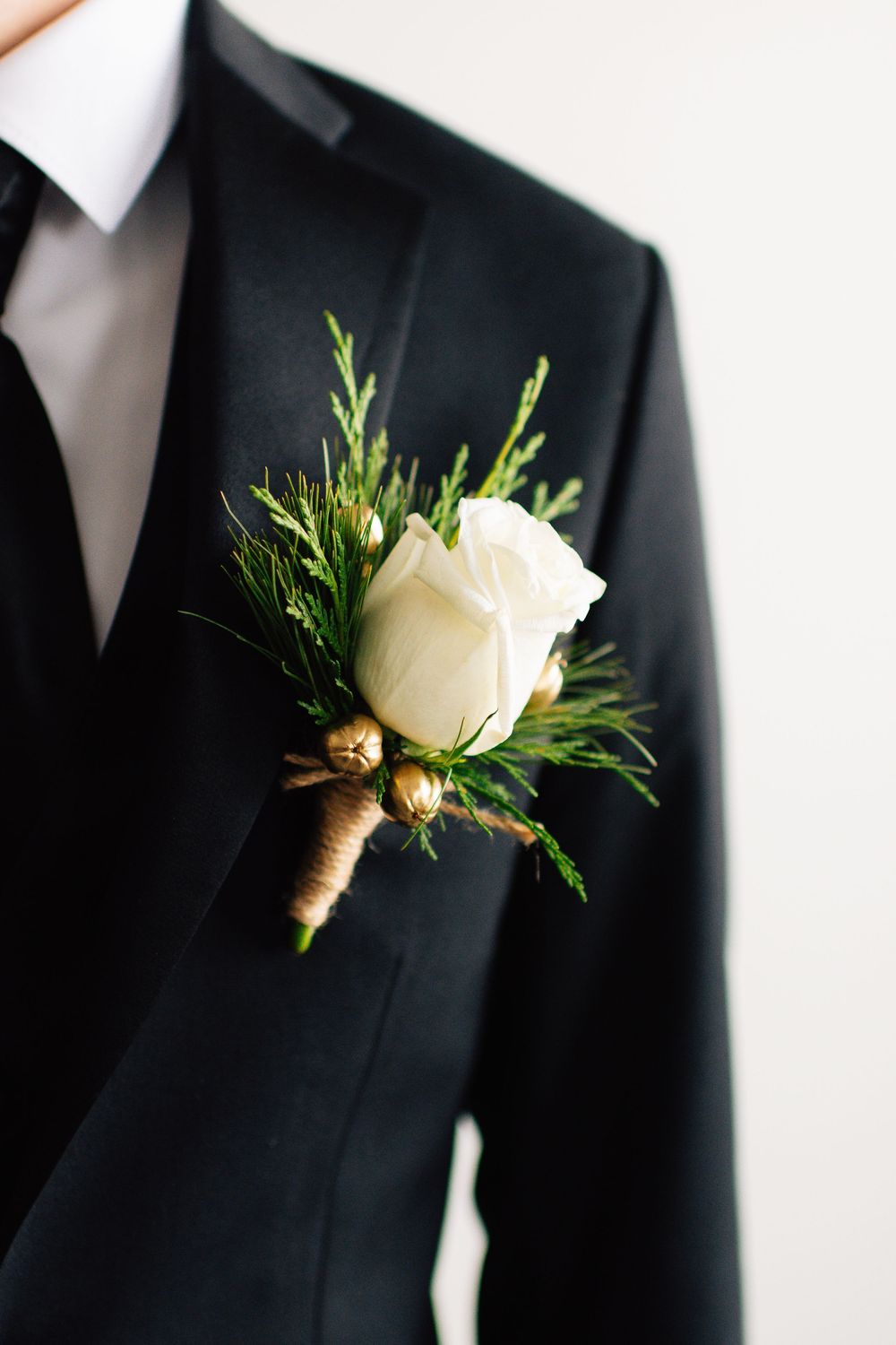 Close-up details of white rose boutonnieres with greenery on black tuxedo lapels.