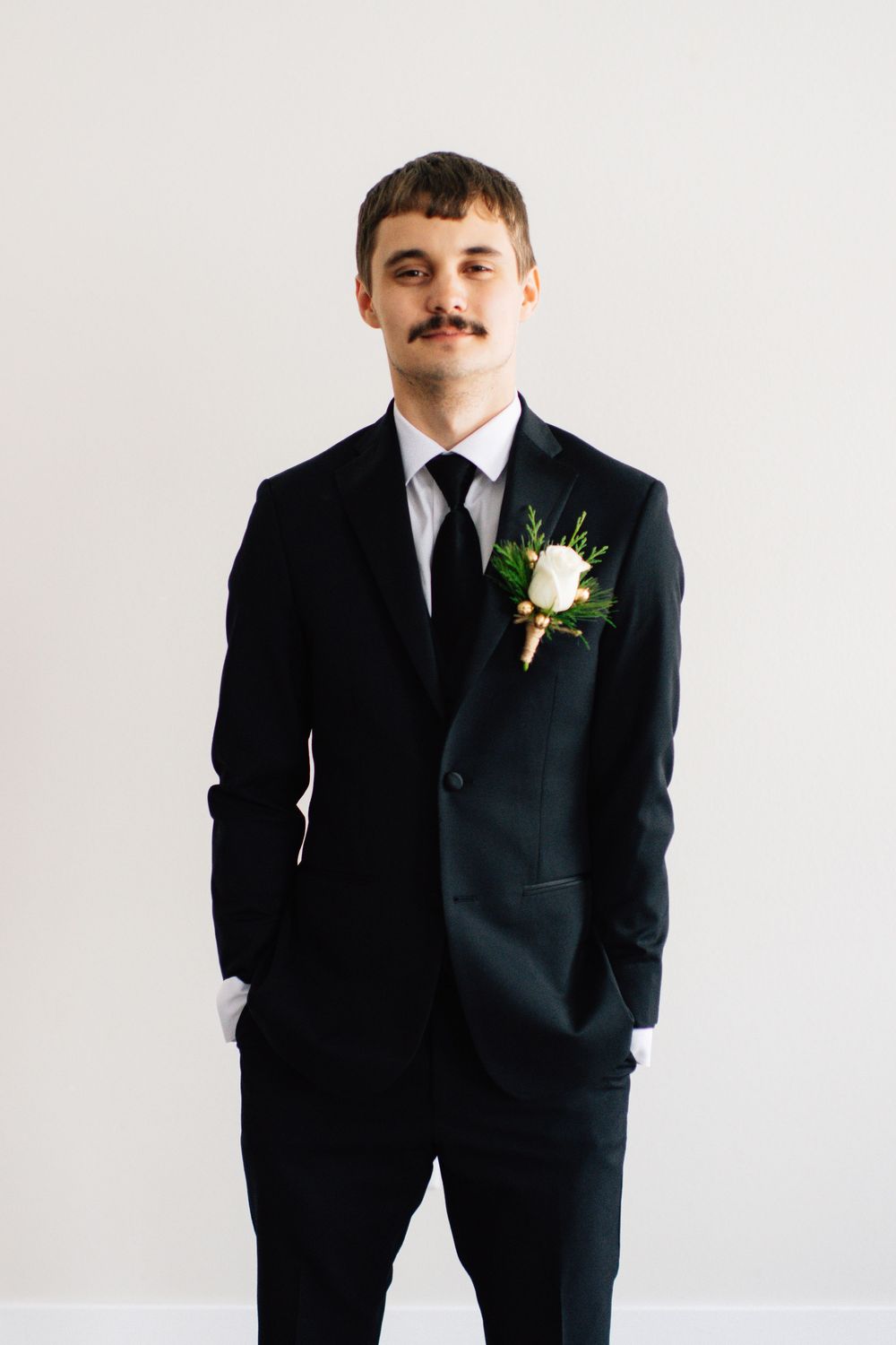 Figure wearing classic black suit and white boutonniere in studio portrait series.