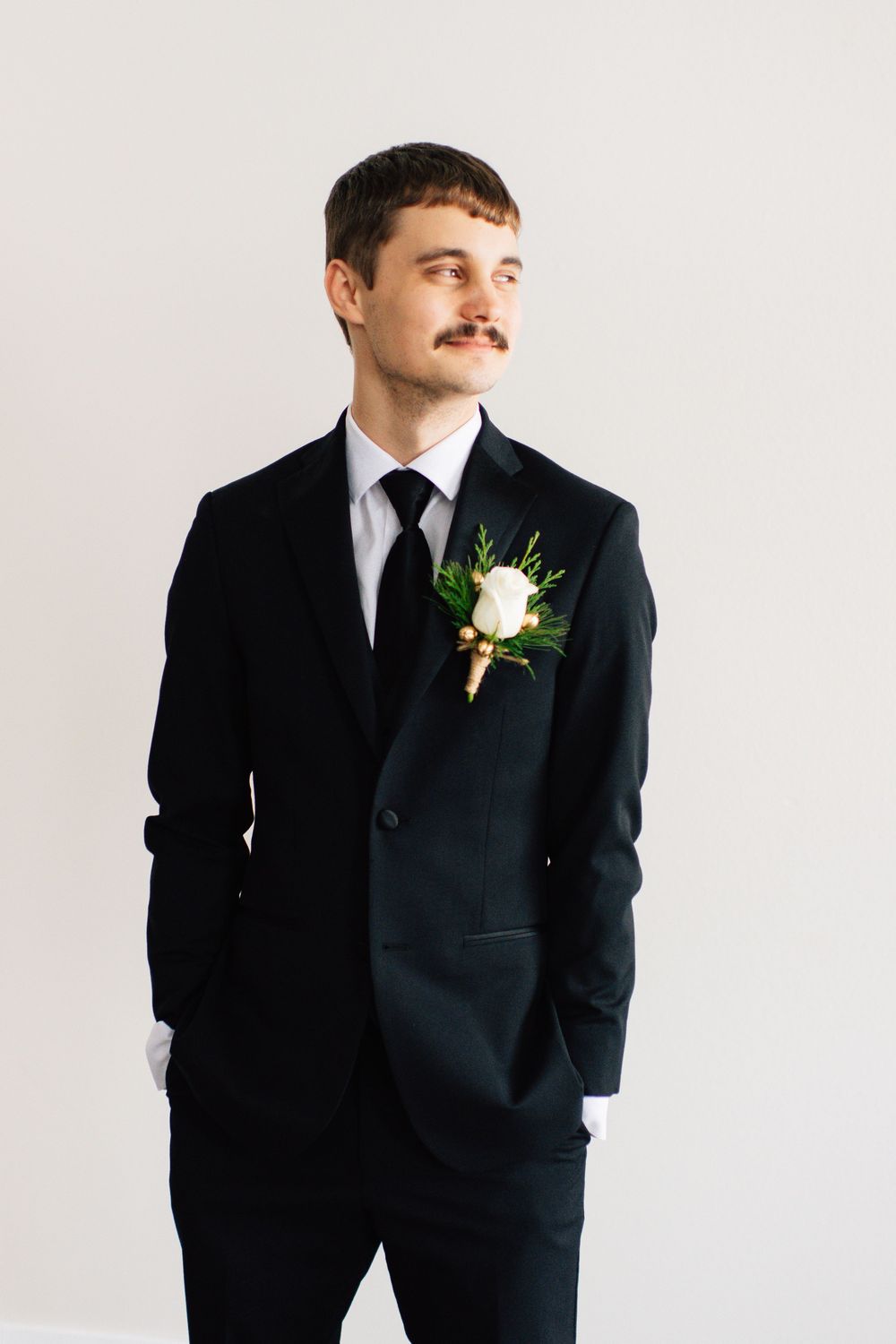 Groomsman in black suit smiles while posing for formal wedding portraits against white background.