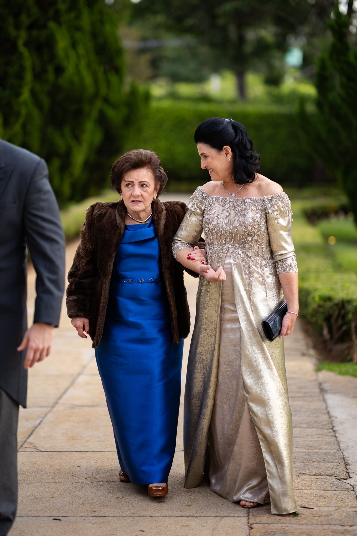 Several people in elegant evening attire gather and share a laugh while standing outdoors.