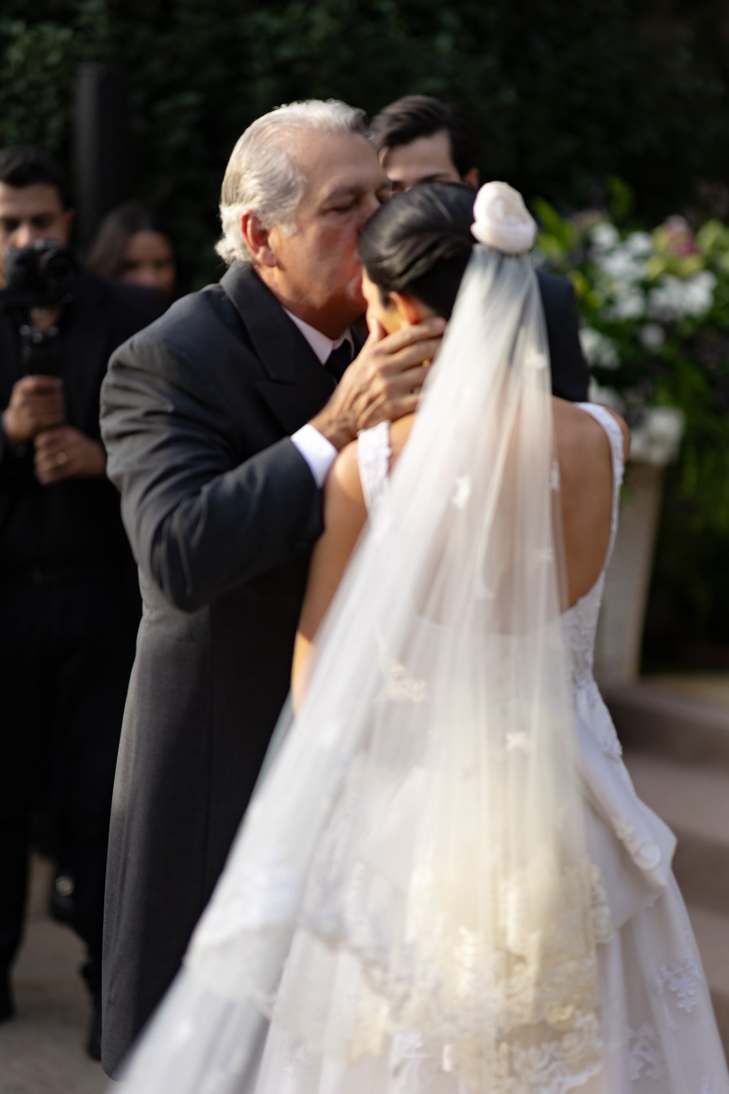 A sequence of wedding photos showing a bride in a flowing white dress and veil being walked down an outdoor aisle.