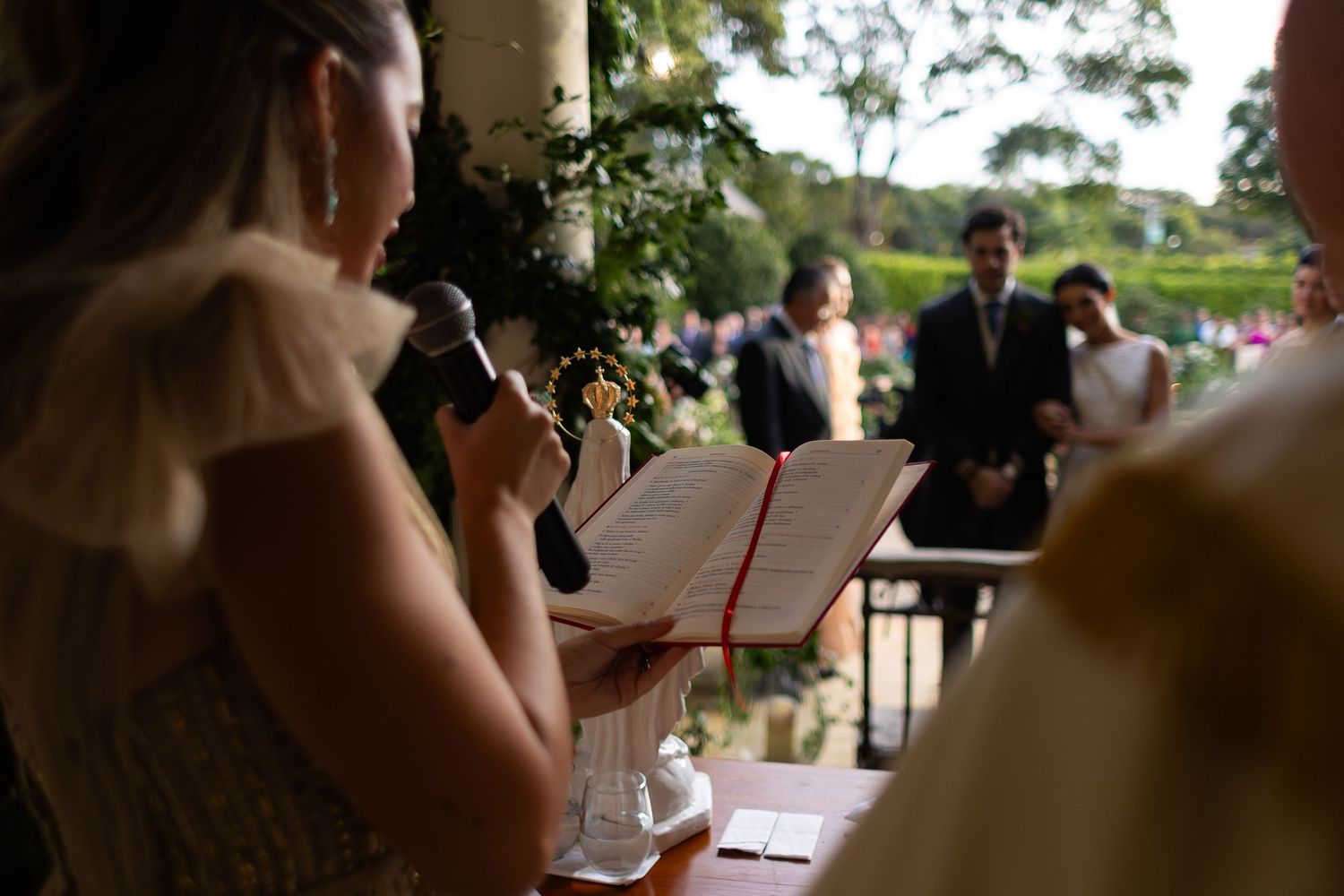 Someone gives a speech from a podium during an outdoor wedding ceremony with guests seated in the background.