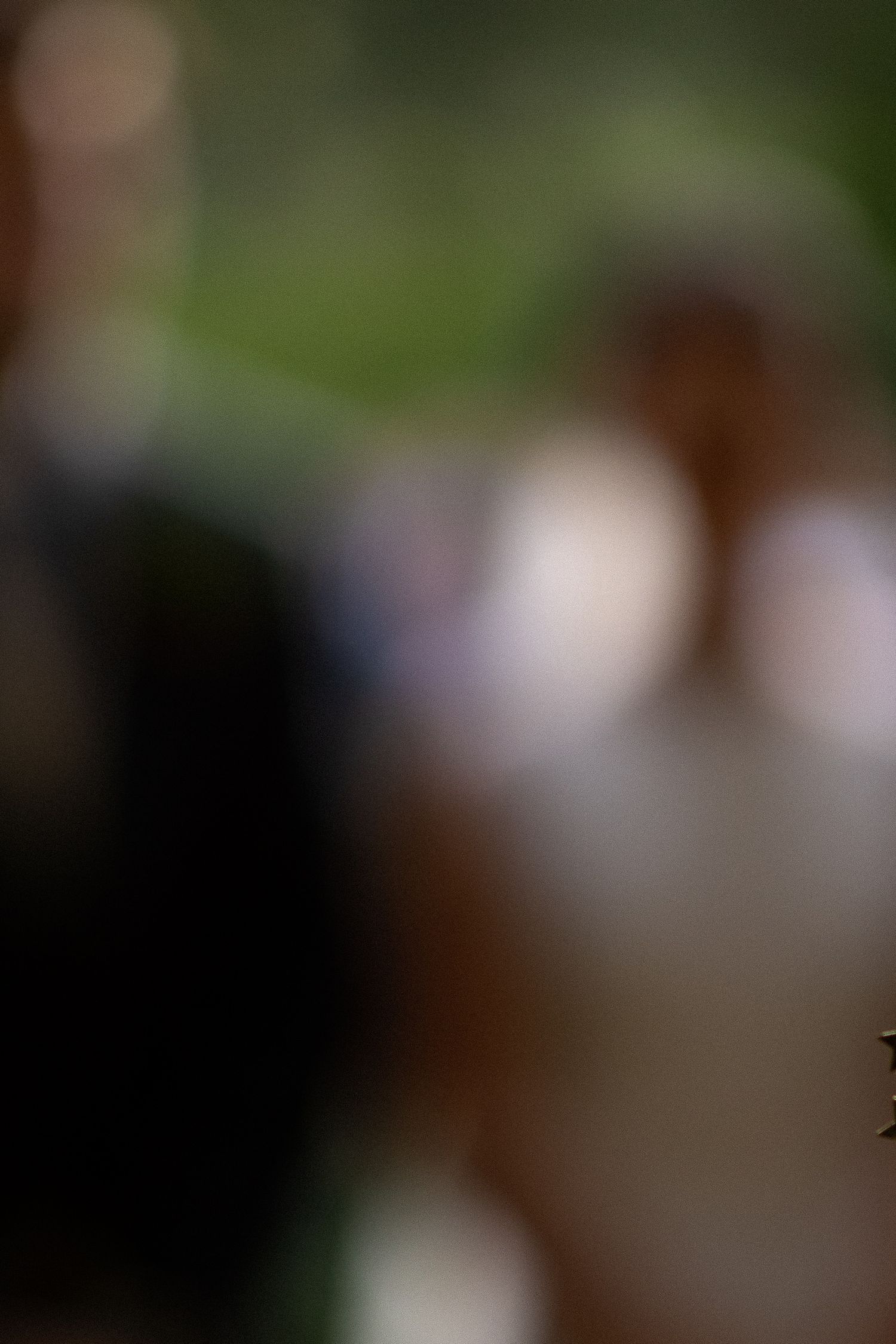 A couple stands together at an outdoor wedding ceremony with a blurred natural background.