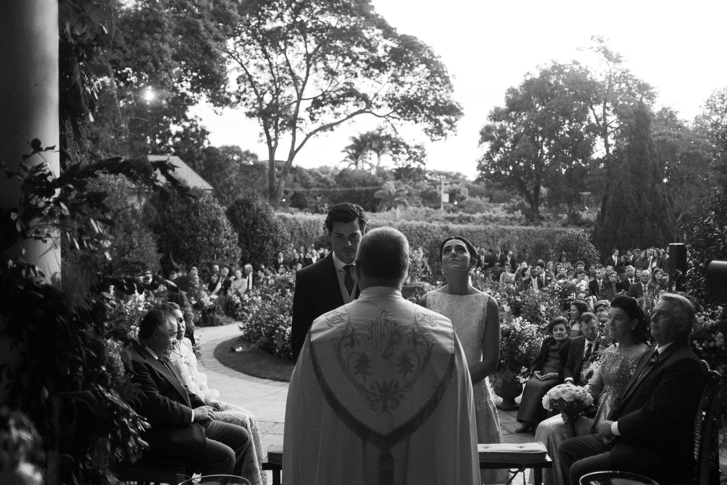 A large crowd gathers outdoors for a special celebration event in a natural garden setting.