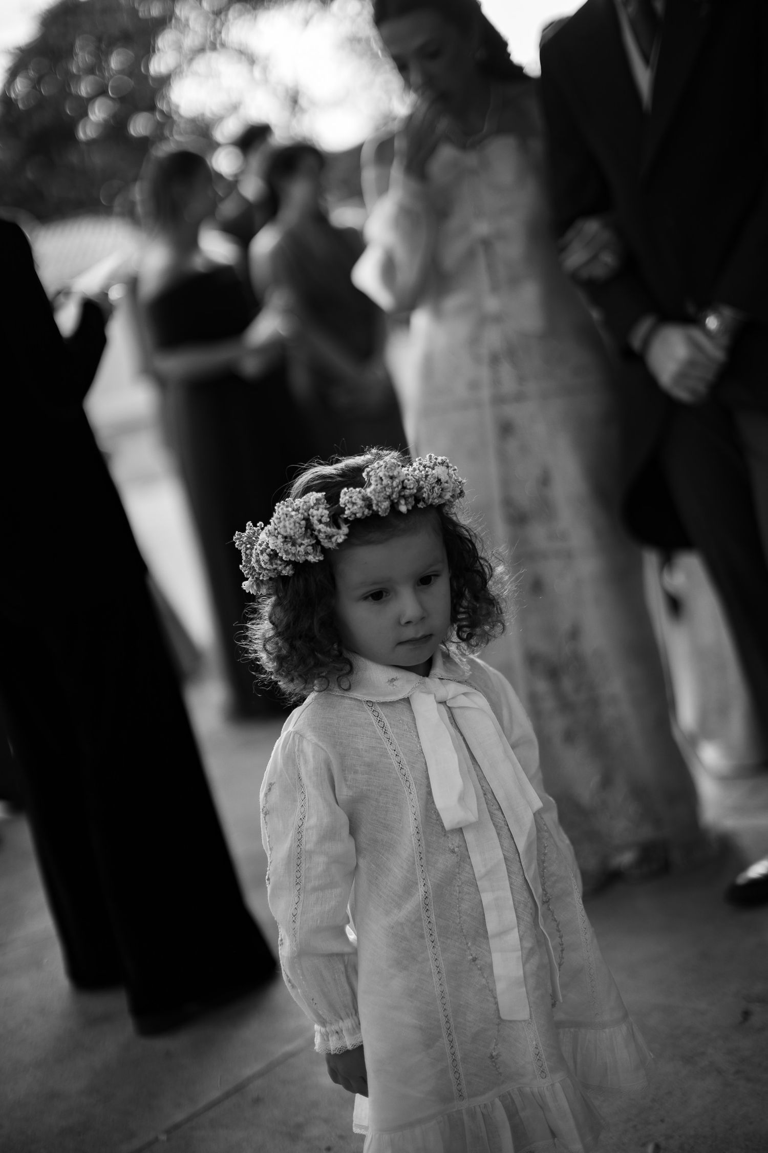 A black and white photograph of a young child in a white dress with curly hair at a formal event.