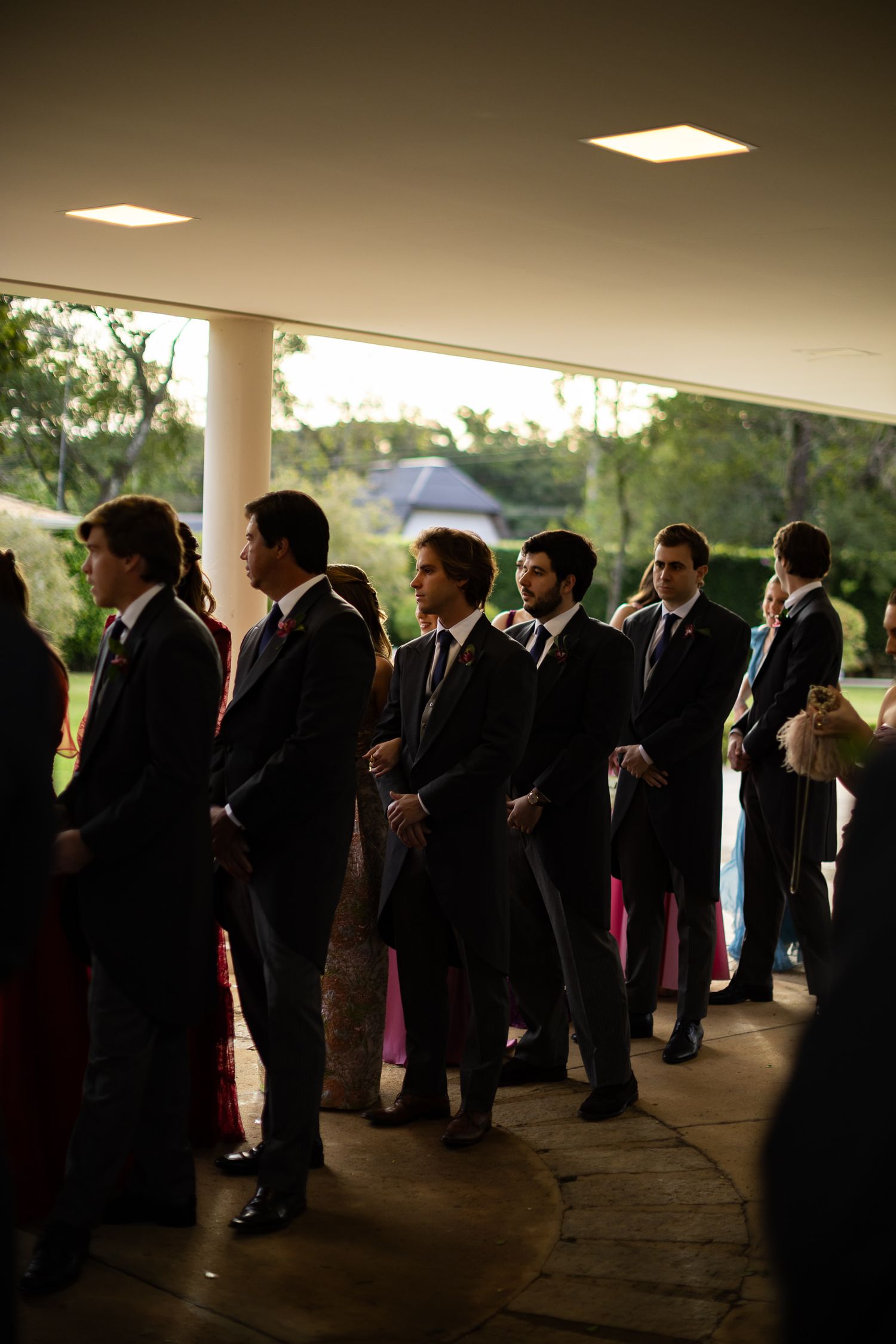 A panoramic view of wedding attendees mingling under a covered pavilion during an evening celebration.