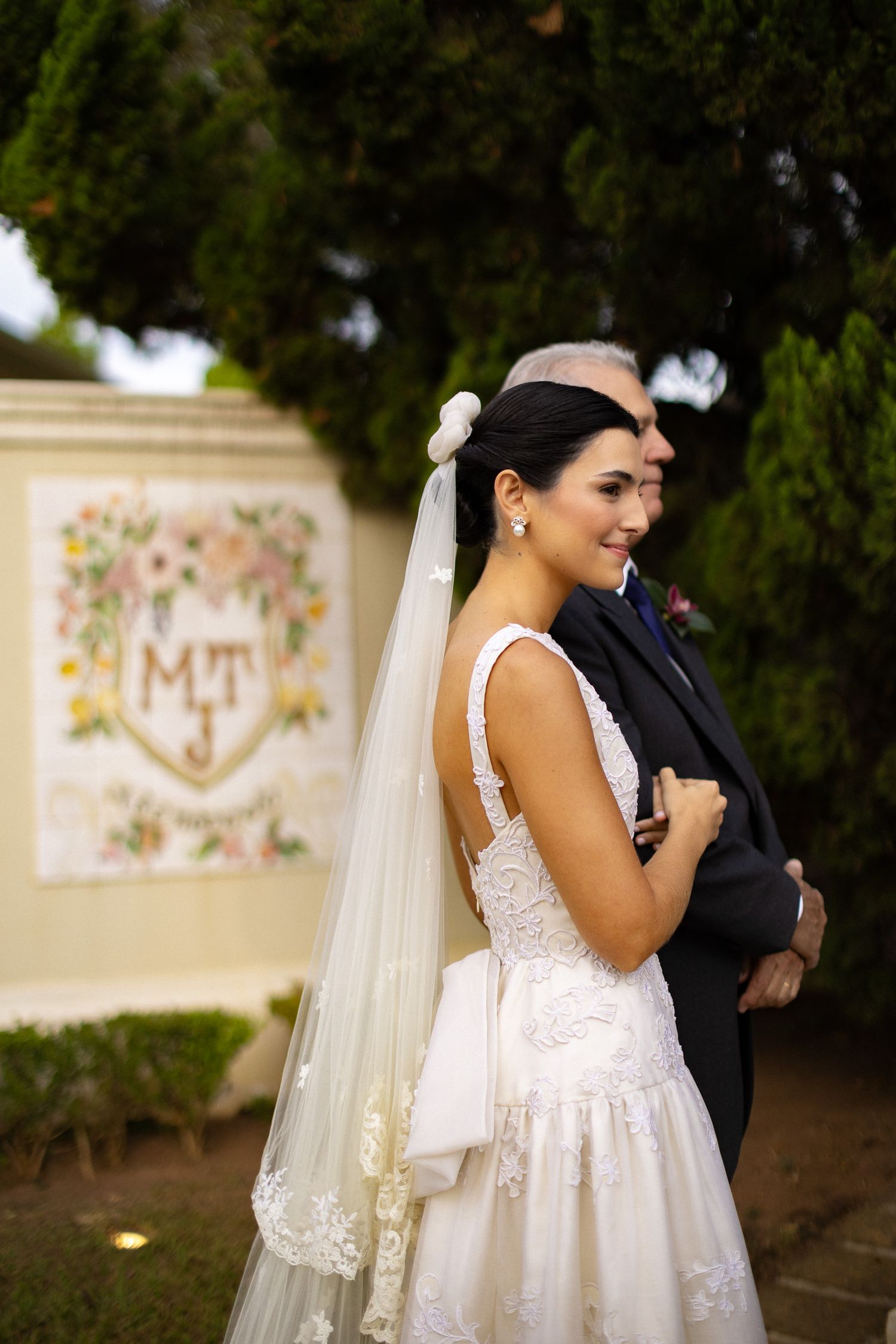 A couple in wedding attire share a joyful moment outdoors with a veil flowing in the breeze.