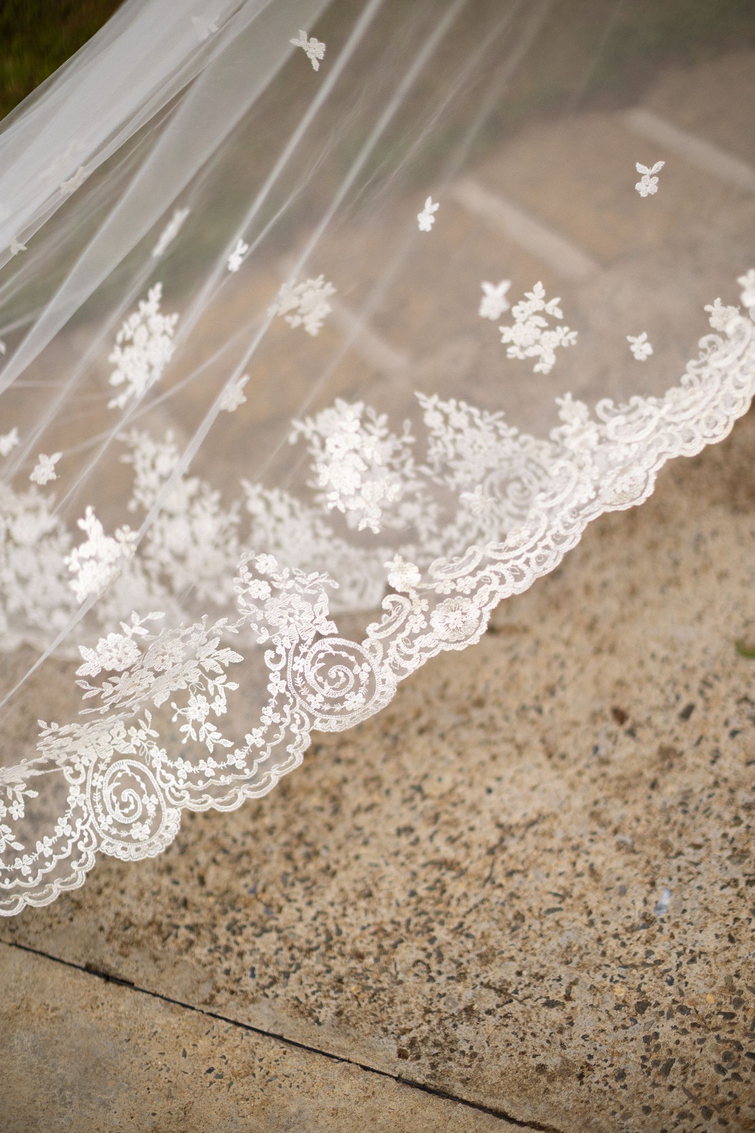 Close-up detail of delicate white lace trim with floral embroidery pattern against a textured stone surface.
