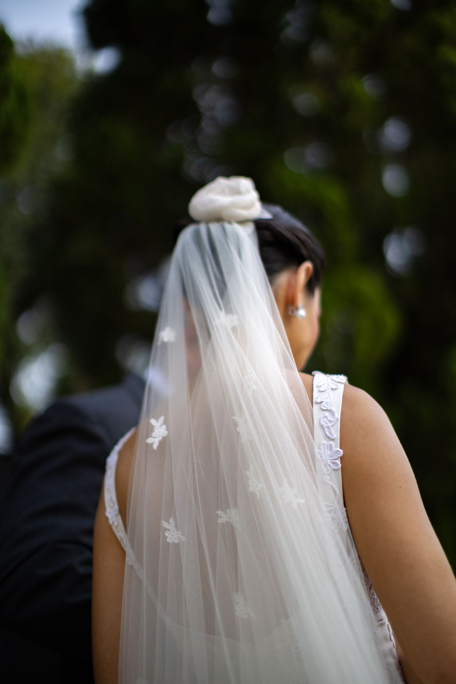 A delicate white bridal veil with floral appliques flows in the wind during an outdoor wedding ceremony.