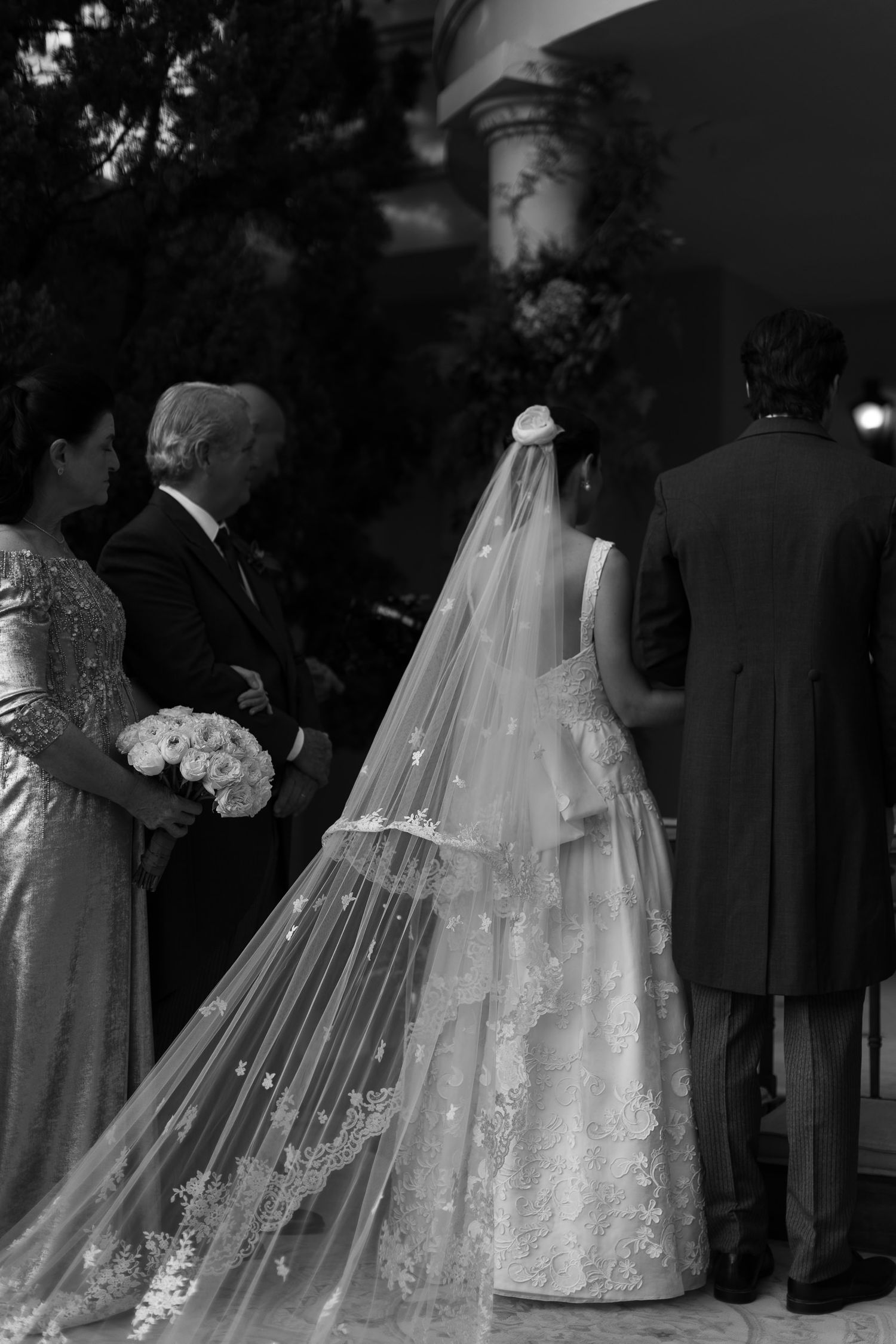 Elegant wedding scene with flowing white lace gown and veil in dramatic black and white photography.