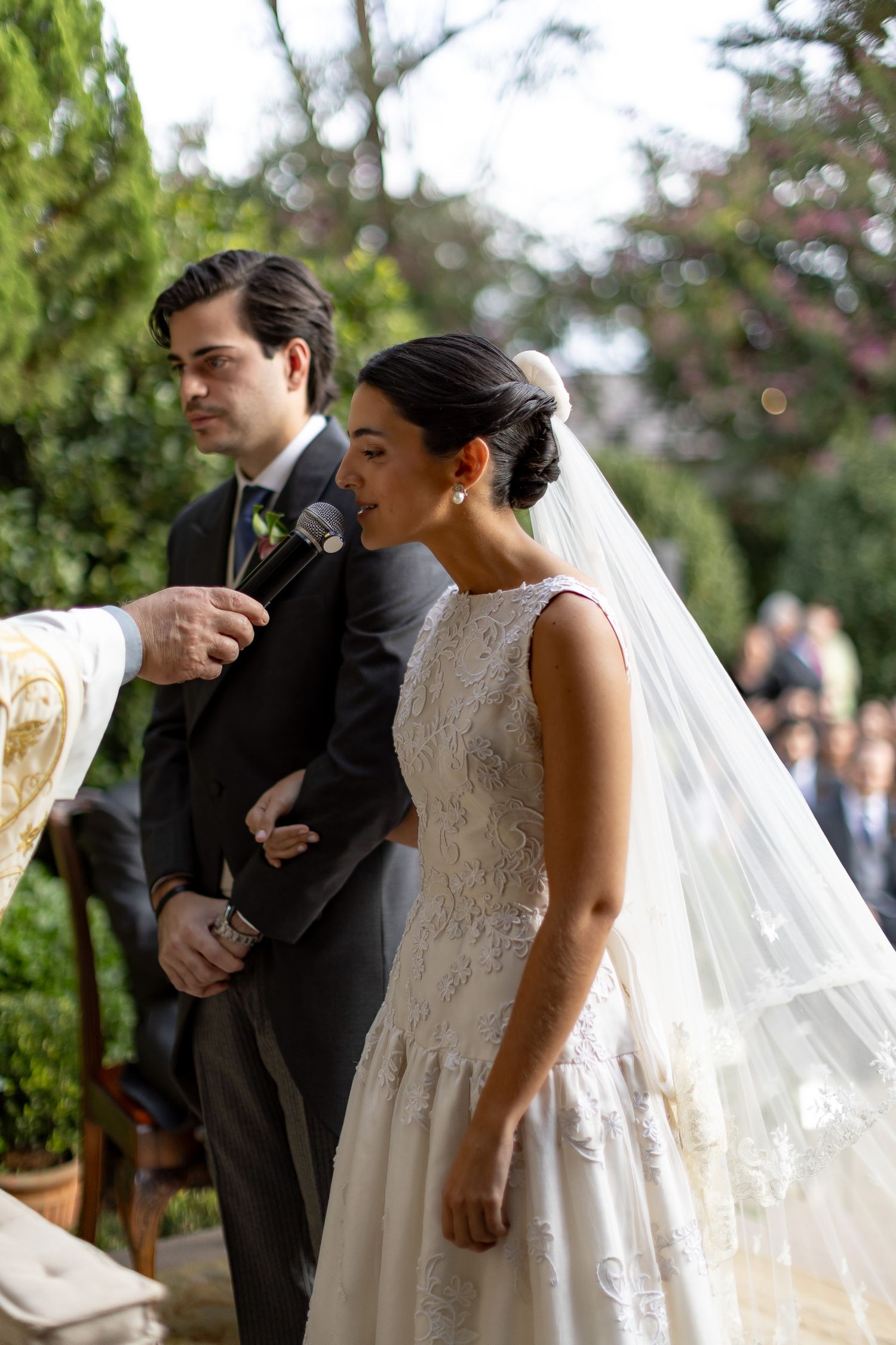 A couple shares an intimate moment during their outdoor wedding ceremony with a flowing white veil in the background.